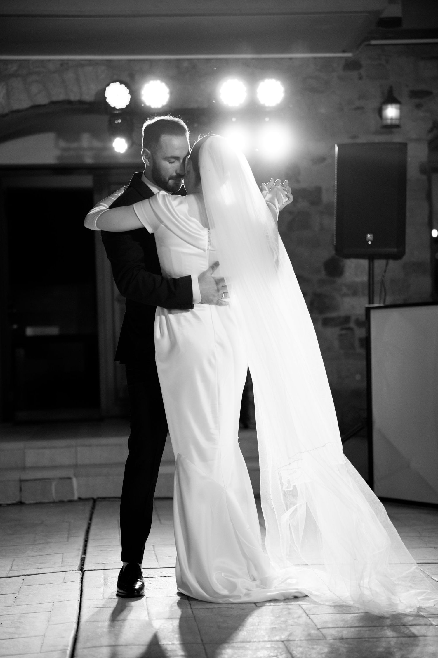 Black and white photo of couple's first dance at wedding reception with dramatic lighting.