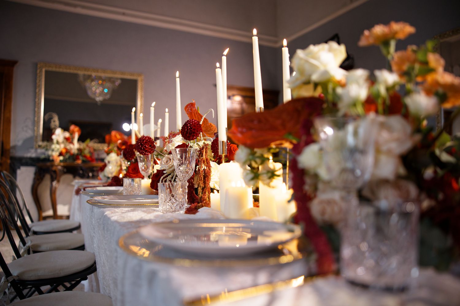 Elegant wedding reception table set with tall white candles and autumn-colored floral arrangements.