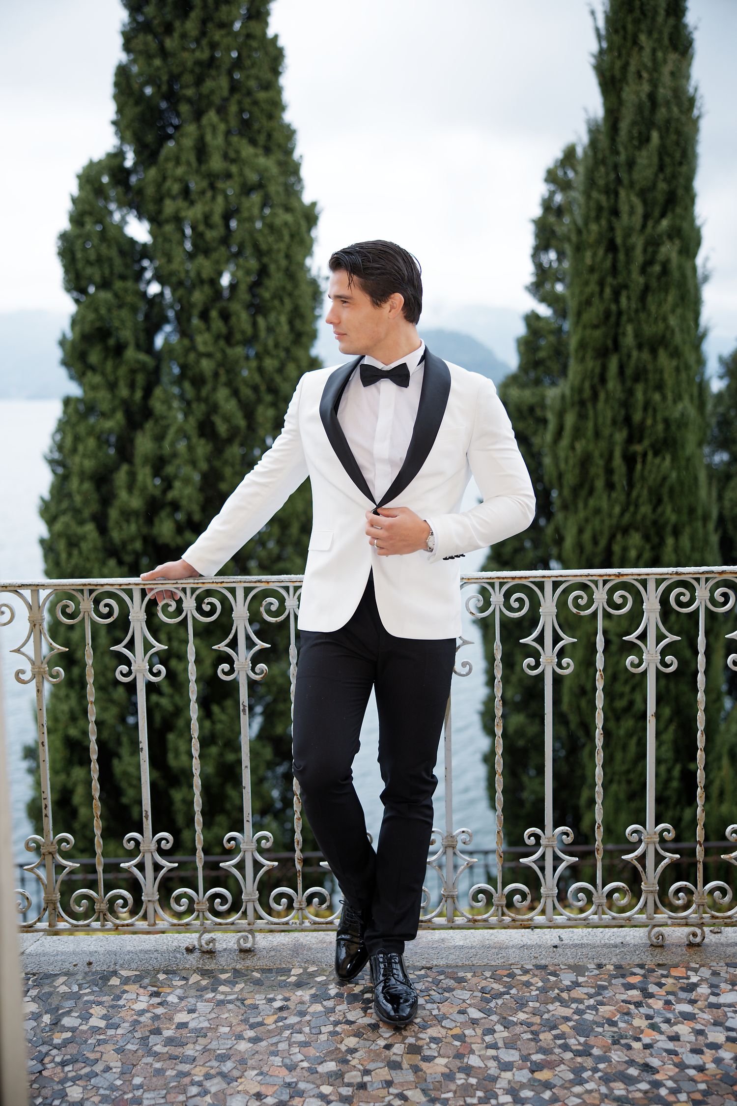 Sophisticated white tuxedo jacket look on ornate balcony overlooking water.