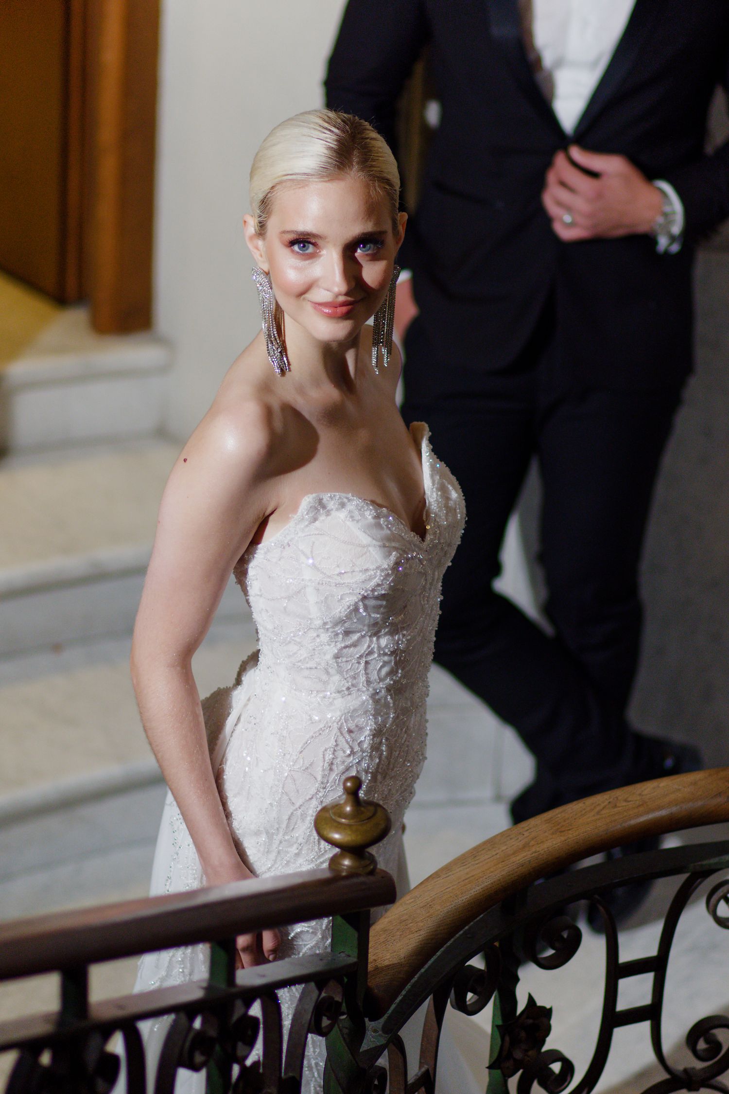 White lace wedding dress with strapless sweetheart neckline and ornate details on elegant staircase.