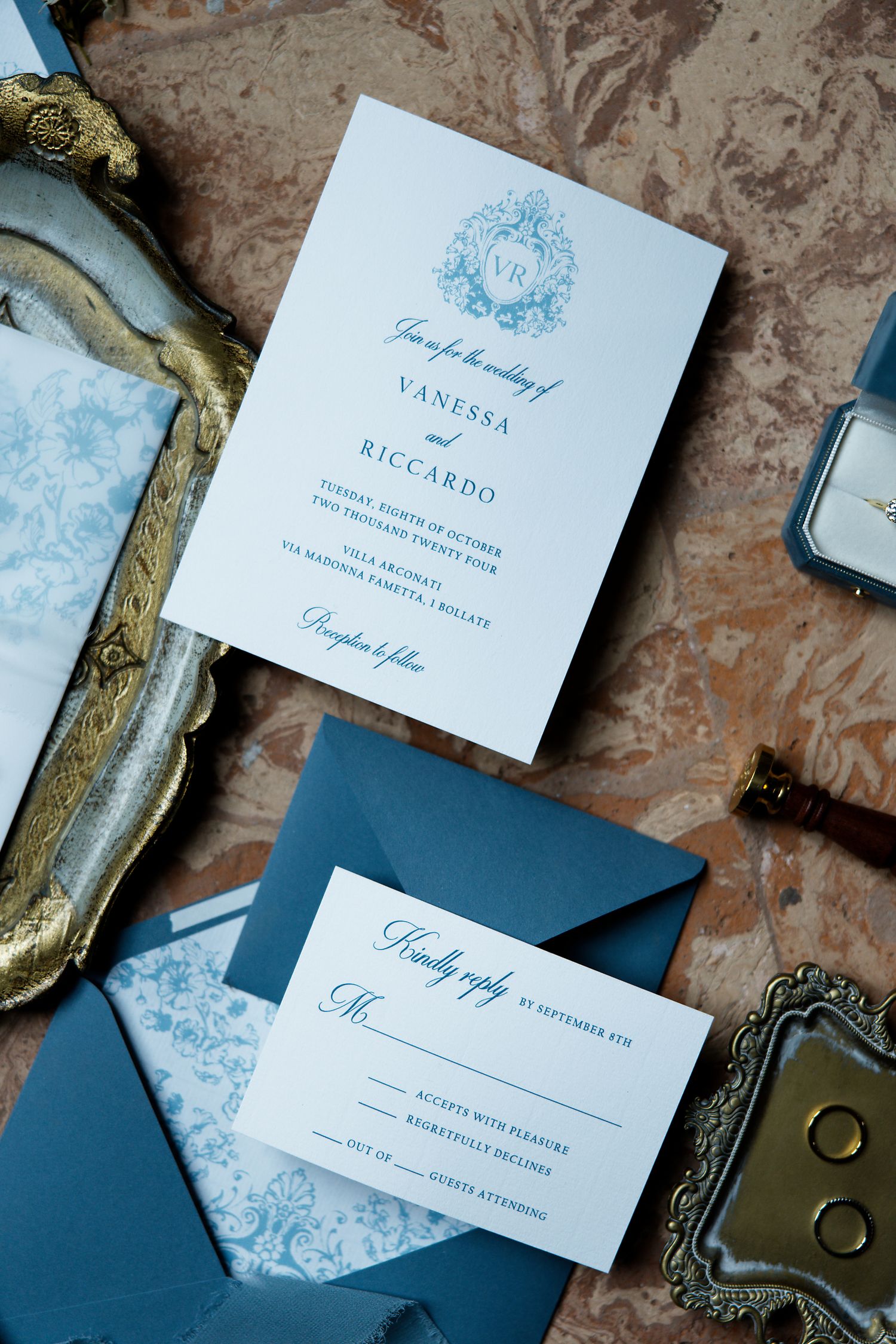 Elegant blue and white wedding invitations with floral motif and matching envelopes on marble surface.