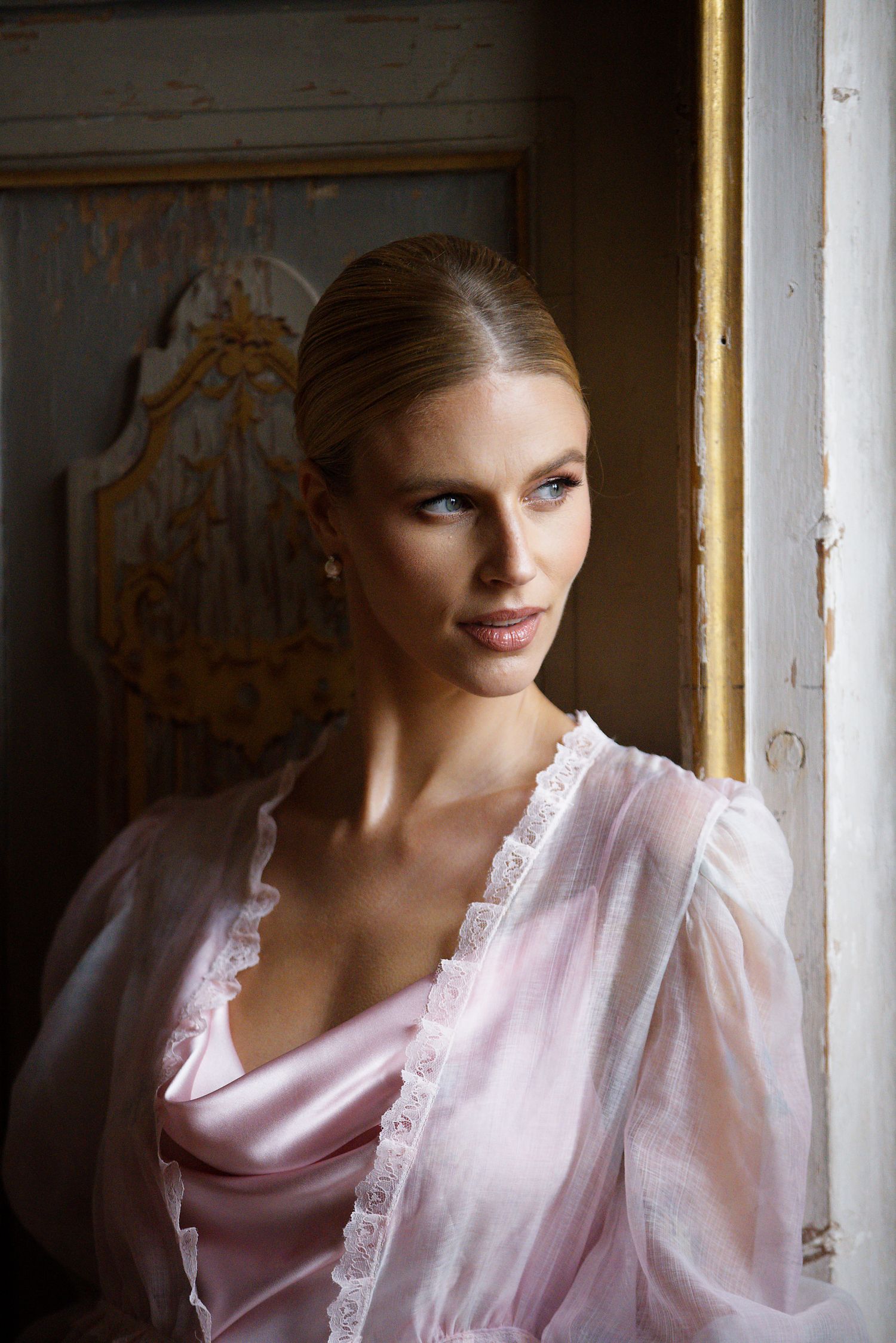 Elegant portrait featuring delicate pink silk dress and classic styling by window.