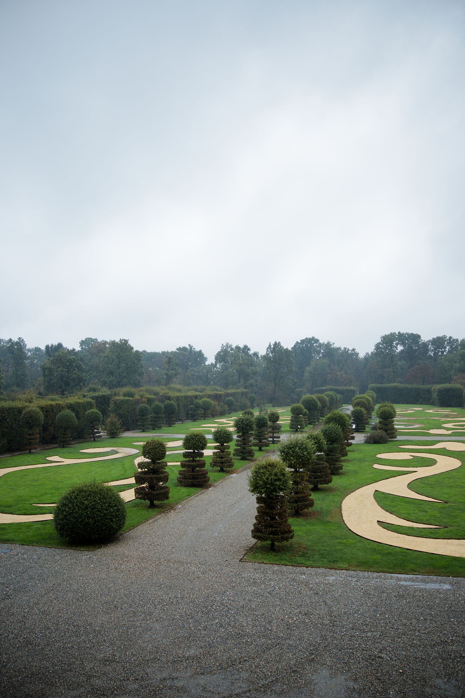 Landscaped garden path with sculptured topiary trees and curved walkways under cloudy sky.