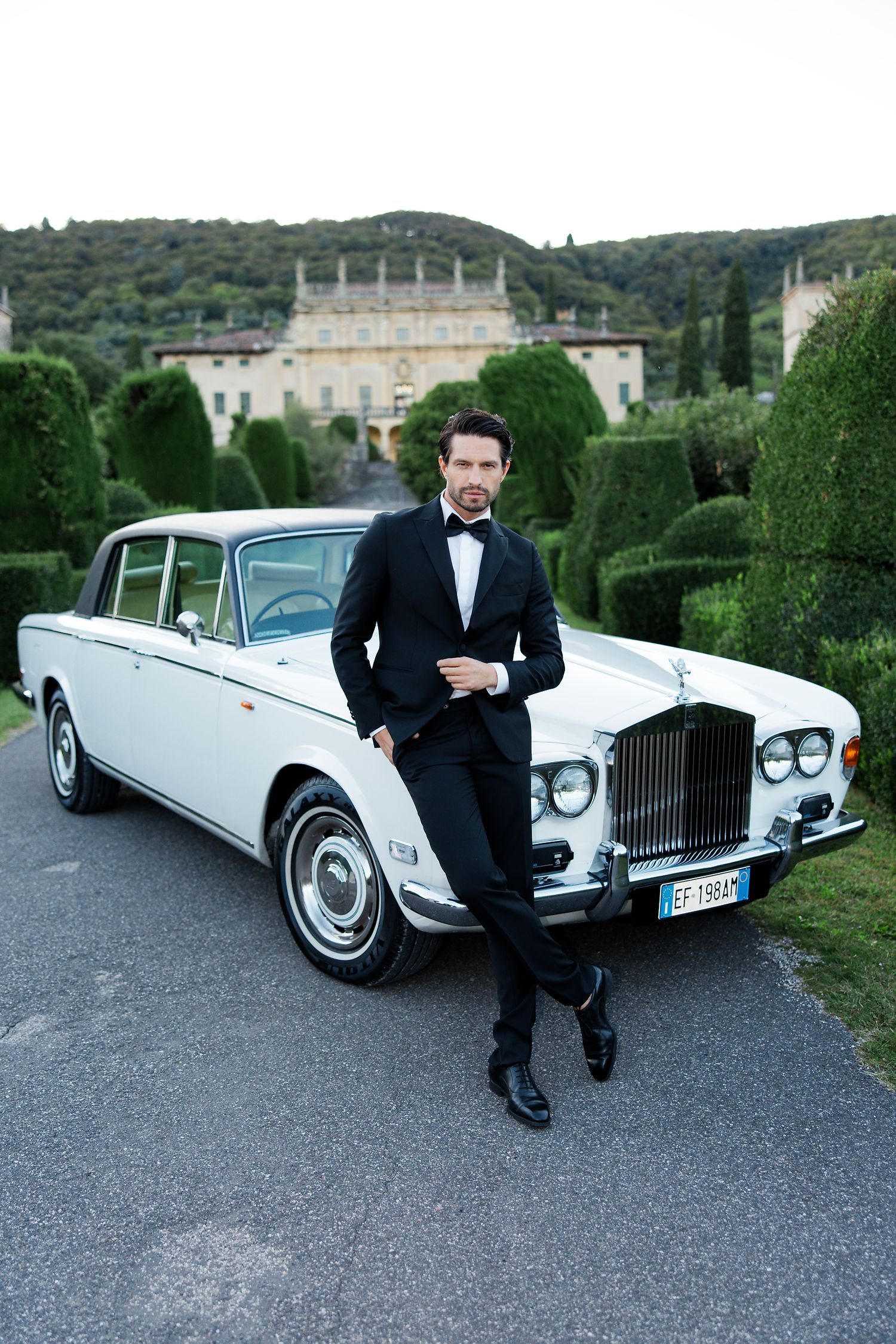 Classic white Rolls-Royce parked in front of an elegant villa with manicured topiary gardens.