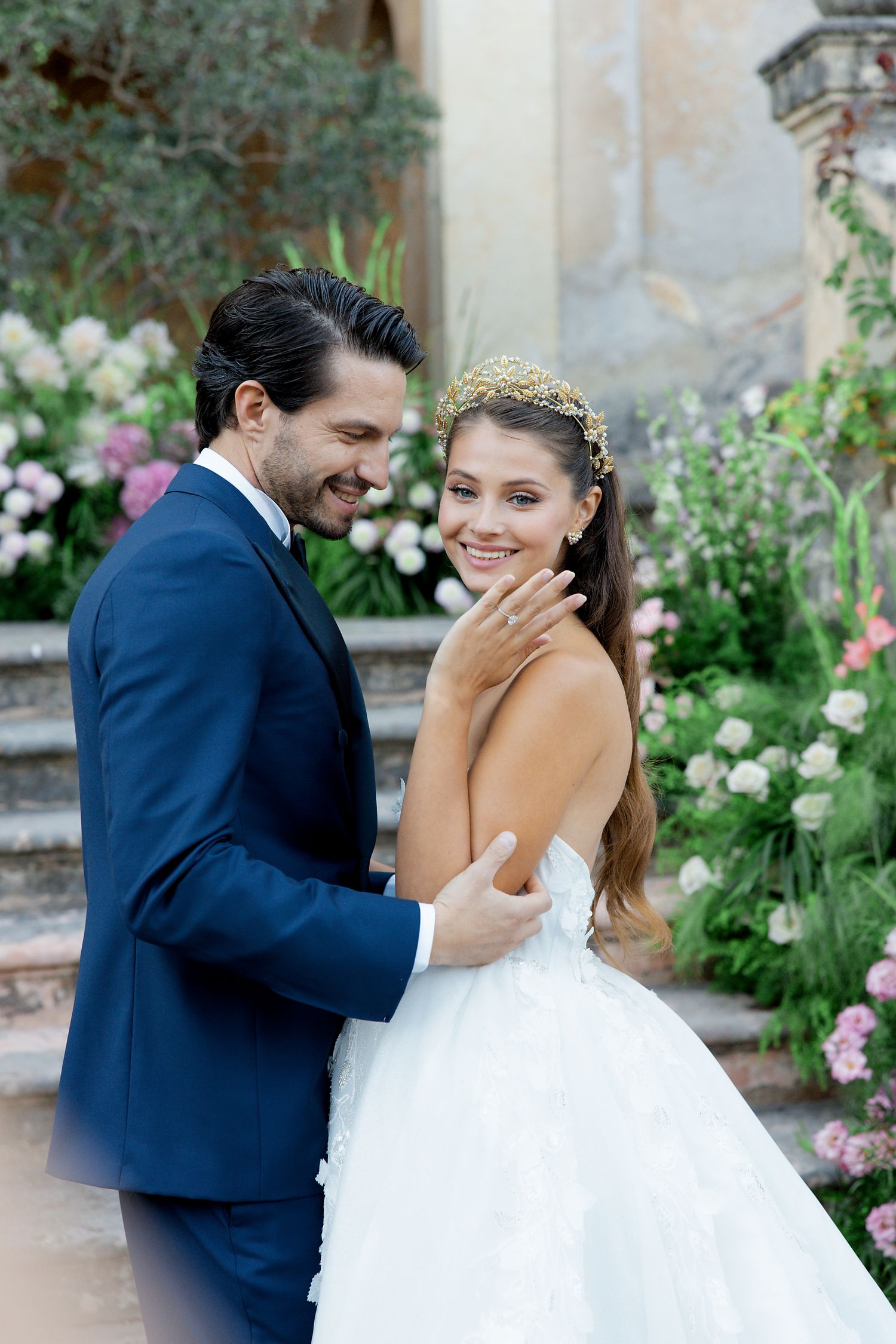 A romantic moment between newlyweds in front of a floral garden staircase.