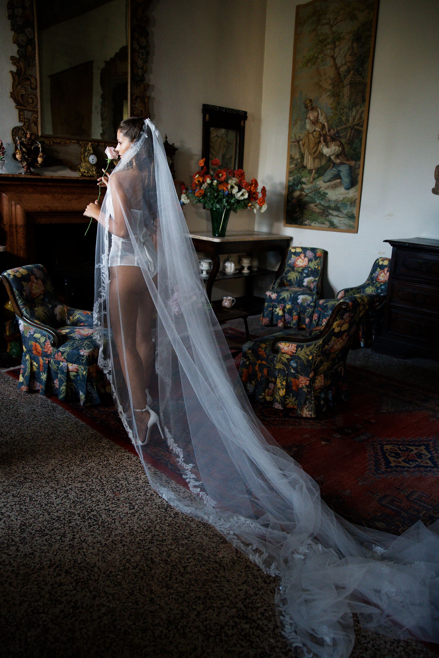 Elegant bridal boudoir photo with long flowing veil in an ornate room with vintage furniture and decor.