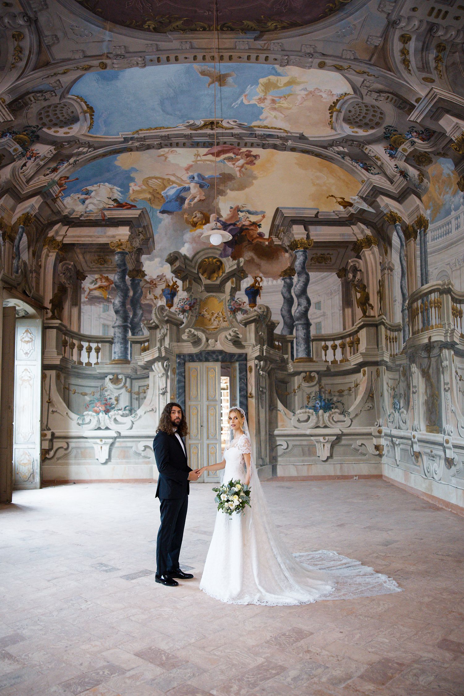 Wedding scene in baroque palace room with stunning frescoed ceiling and ornate architectural details.