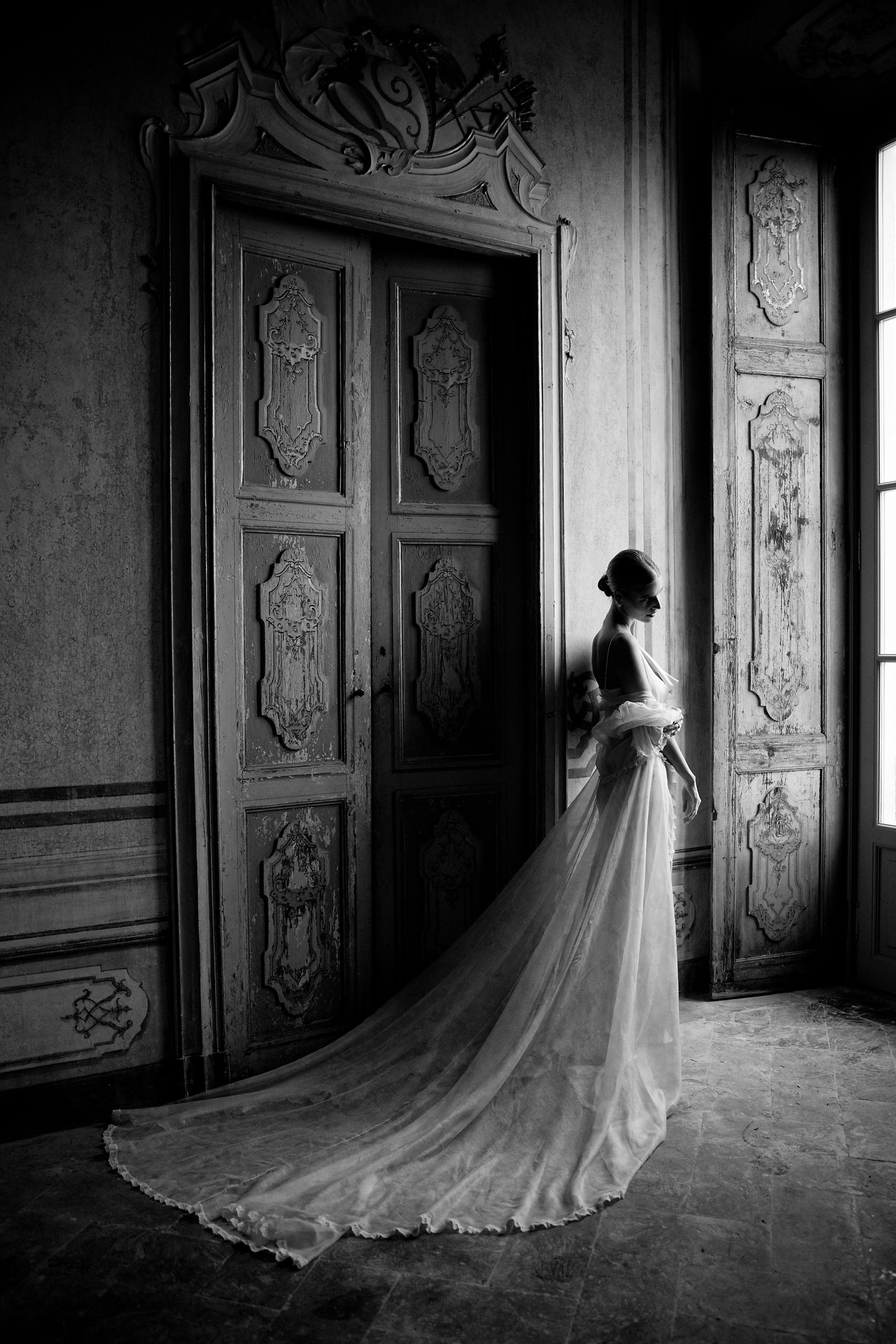 Dramatic black and white silhouette of bride in flowing gown against ornate historical door.