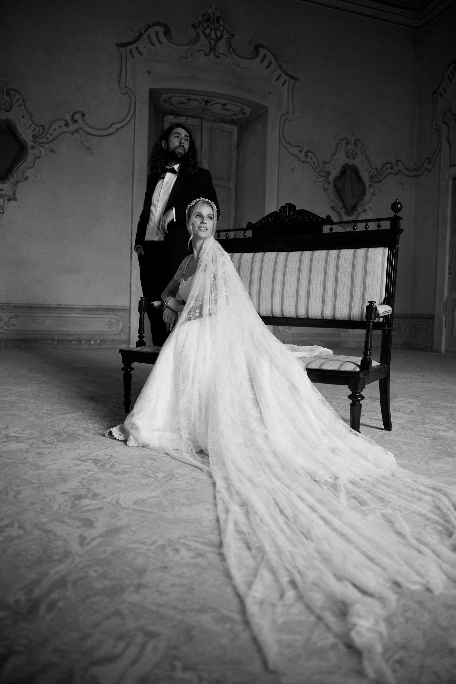 Black and white wedding portrait with couple and flowing dress train in vintage setting.