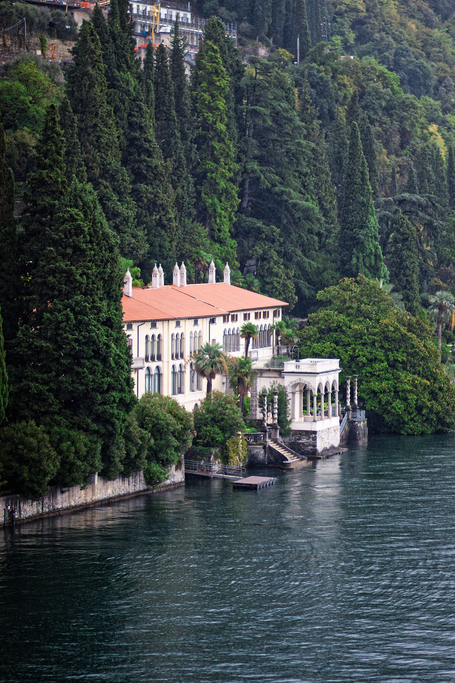 Stunning Italian villa with terrace overlooking Lake Como surrounded by cypress trees.