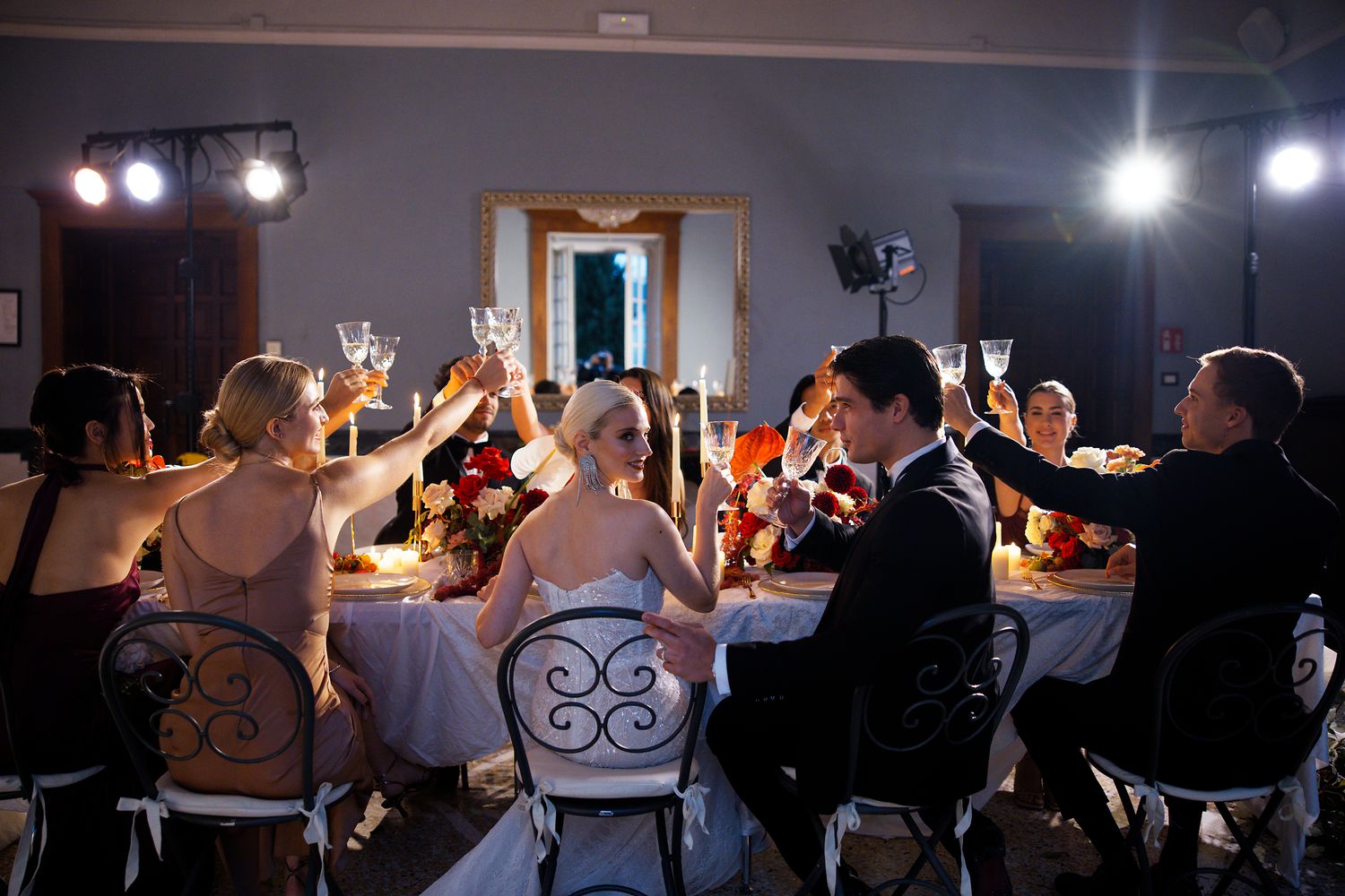 Wedding reception guests raise their glasses for a celebratory toast at a banquet table.