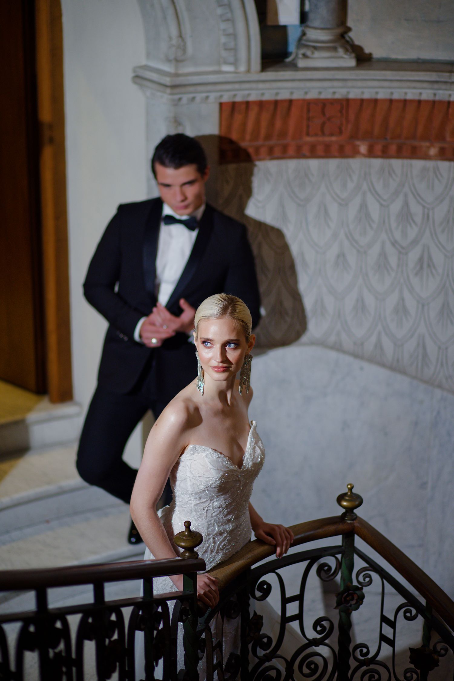Romantic wedding photo on an ornate staircase with decorative ironwork railing.