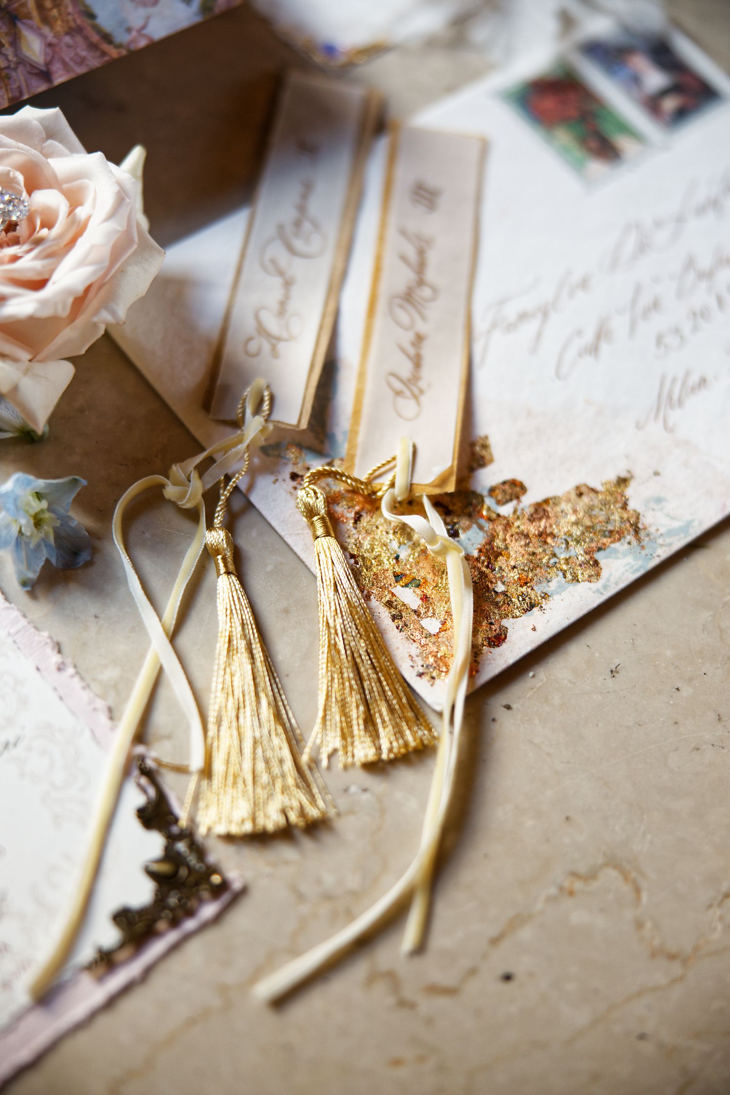 Close-up of gold tassels and blush roses on wedding stationery with handwritten details.