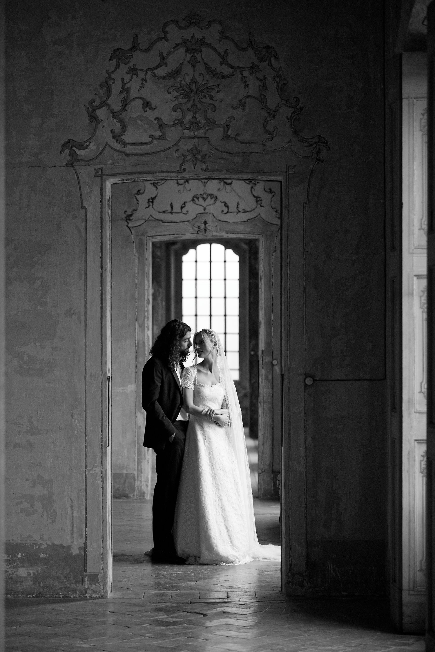 A romantic wedding scene in black and white, showing a couple silhouetted in an ornate doorway with decorative molding.