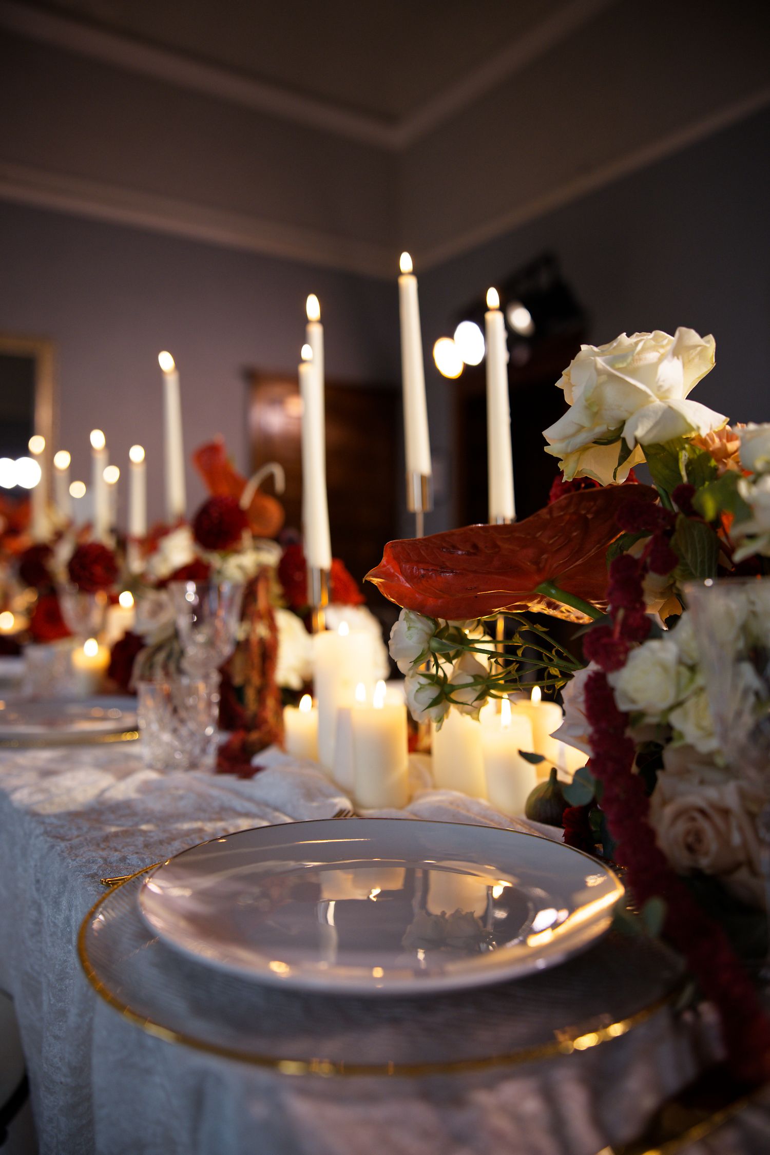 Romantic table setting with glowing candles, roses and fine china at elegant wedding reception.