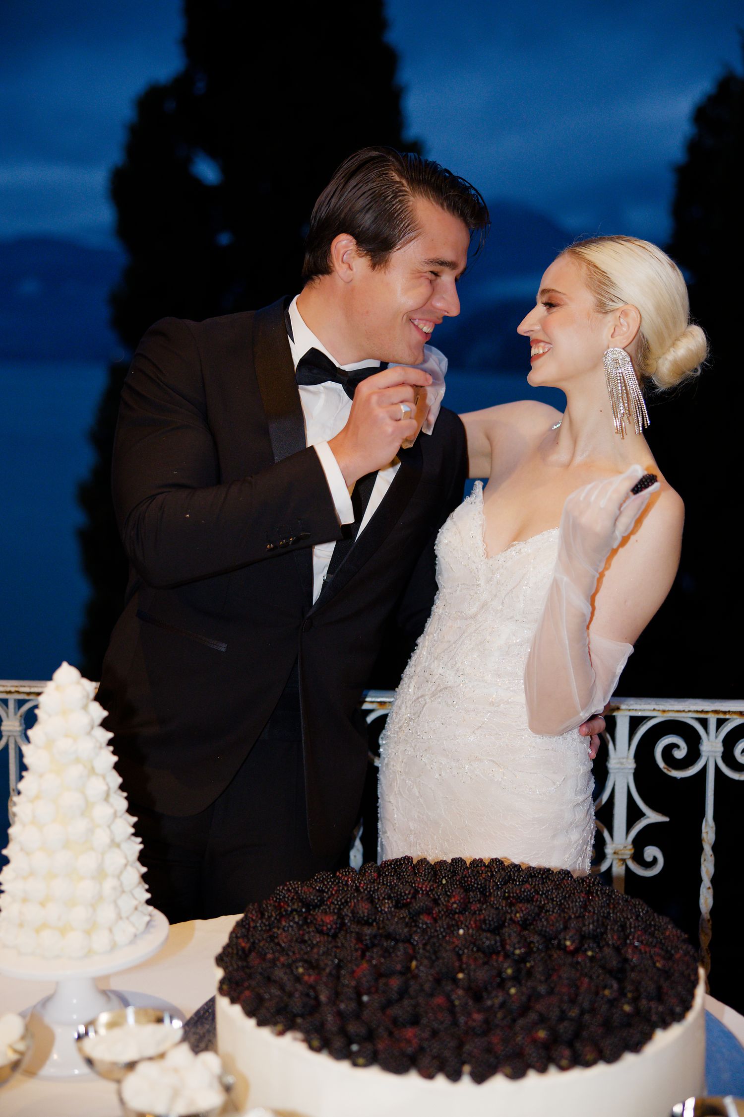 Newlyweds share a joyful moment near their wedding cake display at an evening reception.