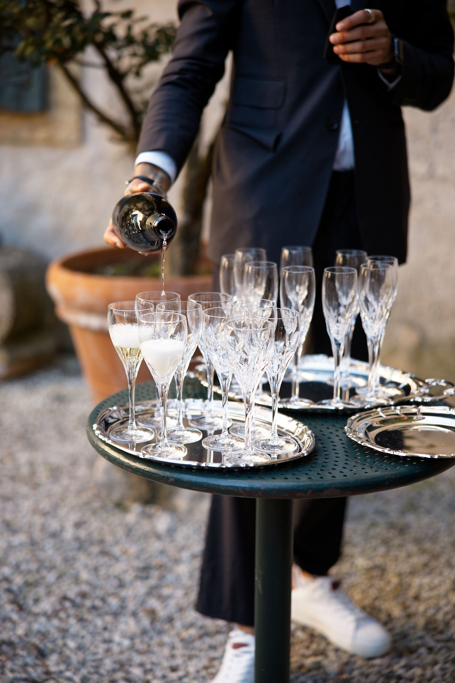 Champagne being poured into crystal glasses on an elegant serving tray at an outdoor event.