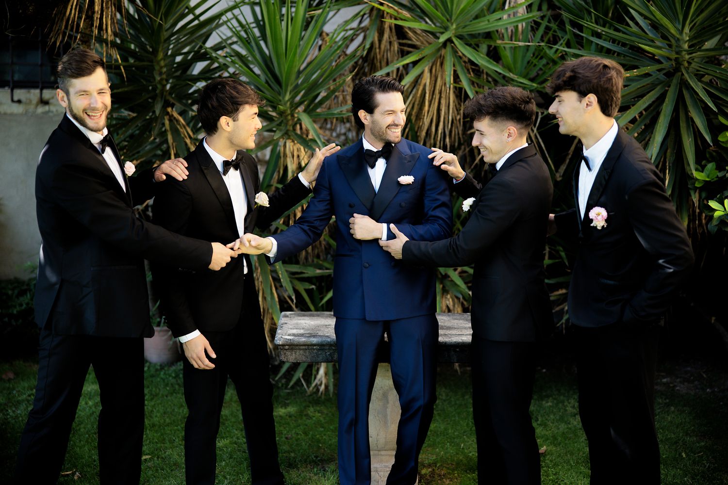 Groomsmen in formal tuxedos sharing laughs during wedding celebration.