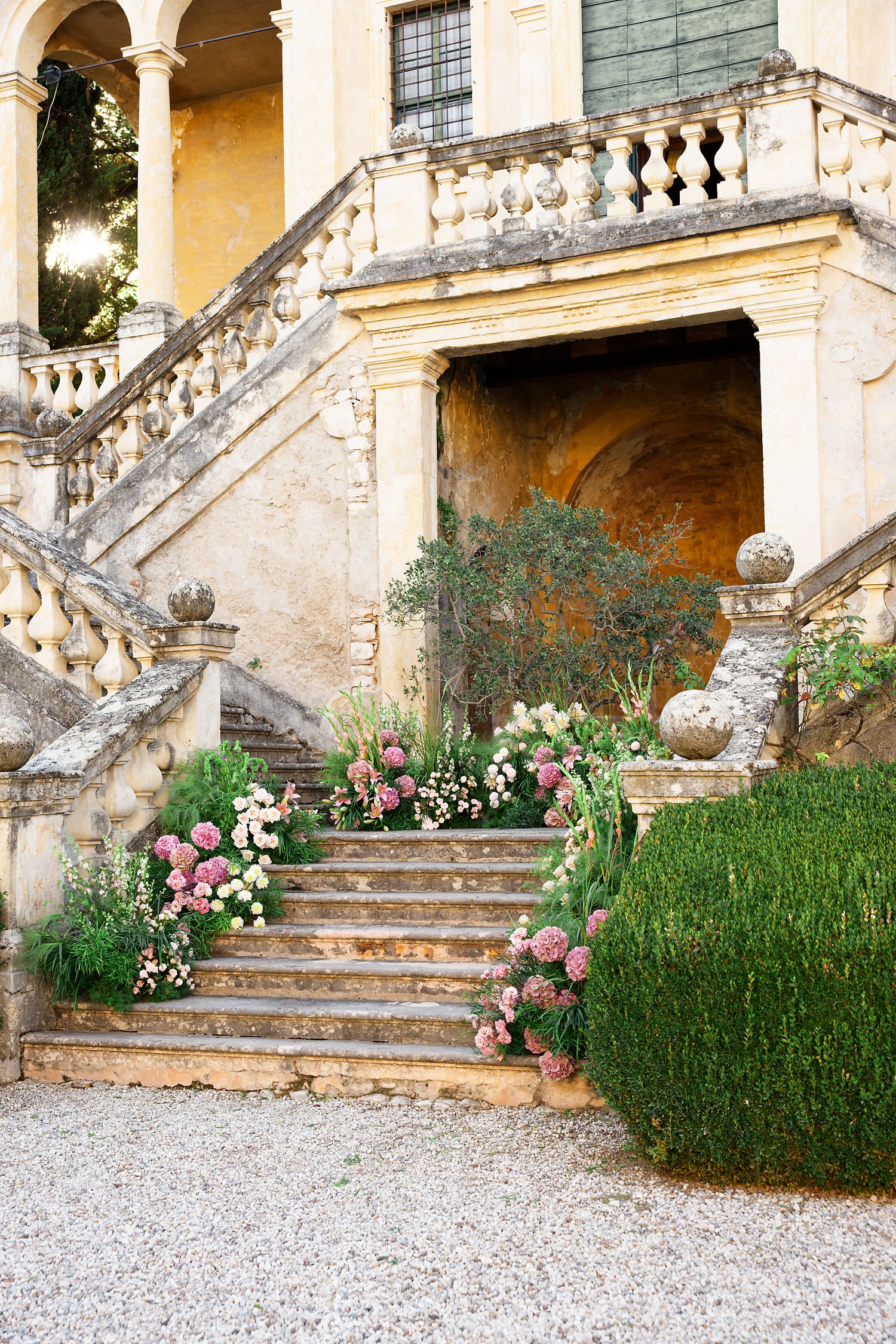 Stone staircase adorned with pink flowers and greenery at an elegant villa entrance.