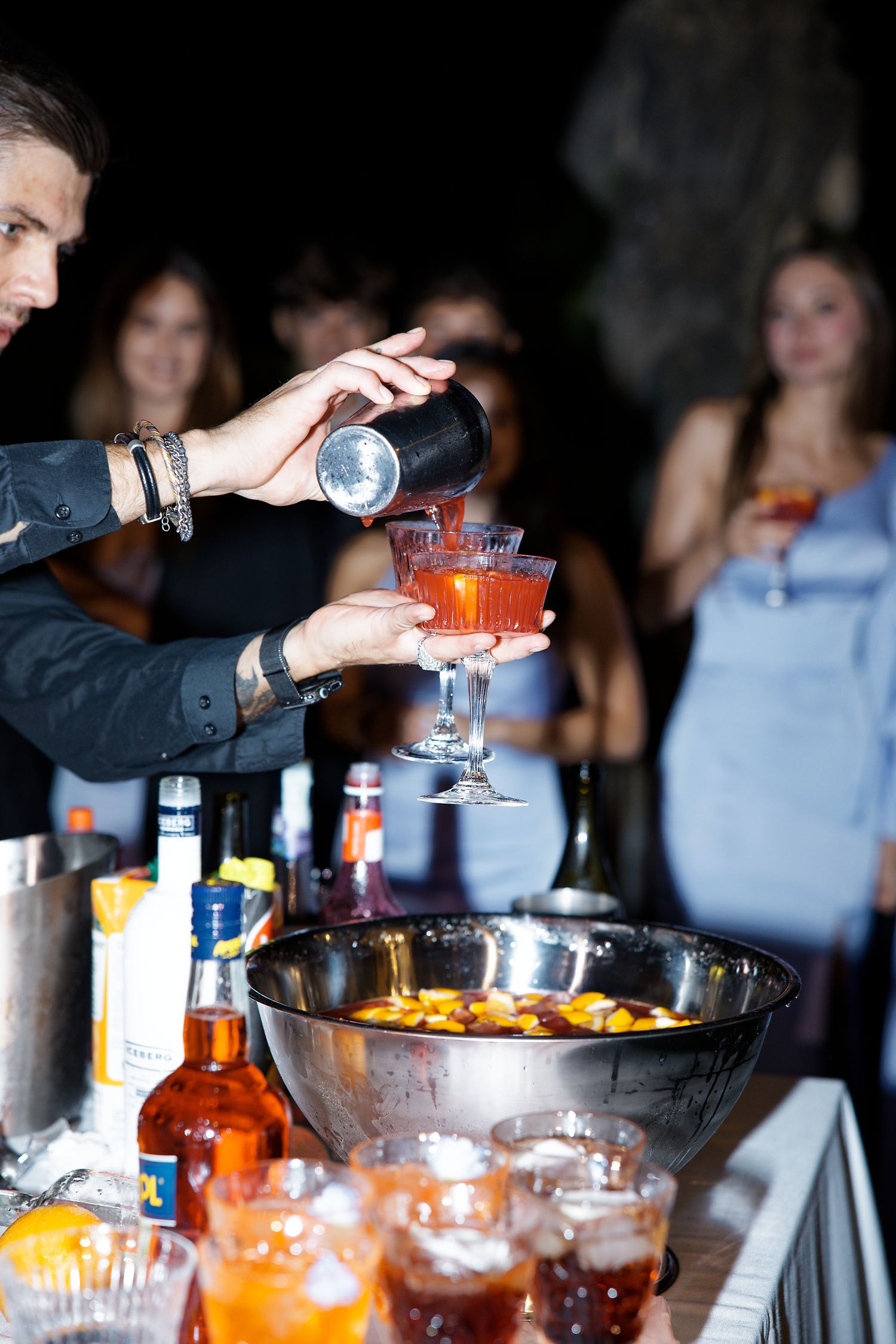 Bartender pouring cocktails at an elegant party with a punch bowl and various bottles on the bar setup.