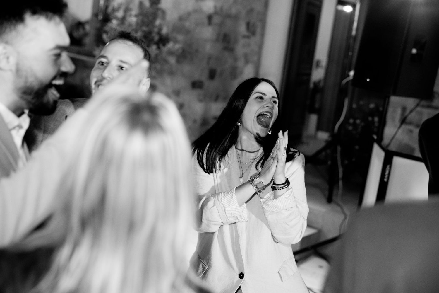 A candid black and white photo captures excited wedding guests laughing and reacting with joyful expressions.