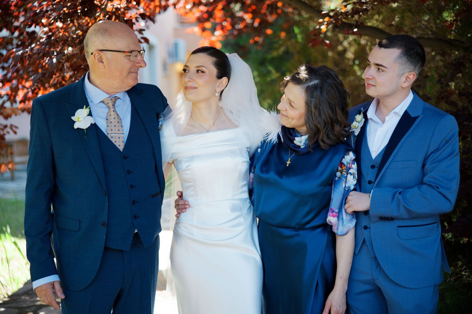 A formal outdoor wedding moment captured against autumn foliage with elegantly dressed people in navy and white.