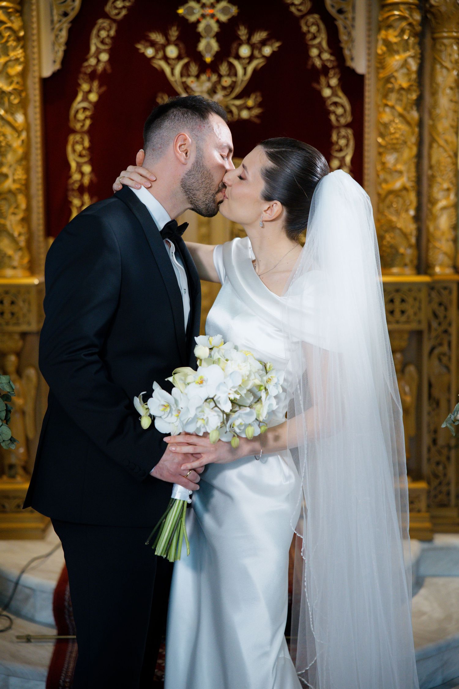Romantic wedding ceremony in an ornate gold-decorated church with white floral bouquets.