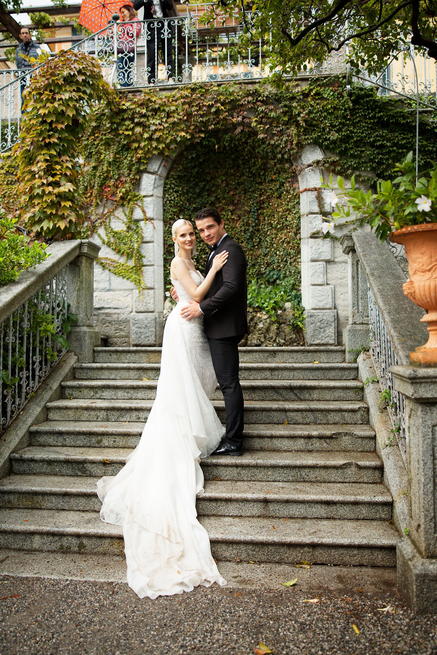 A romantic wedding photo on elegant stone stairs covered in ivy at a grand estate.