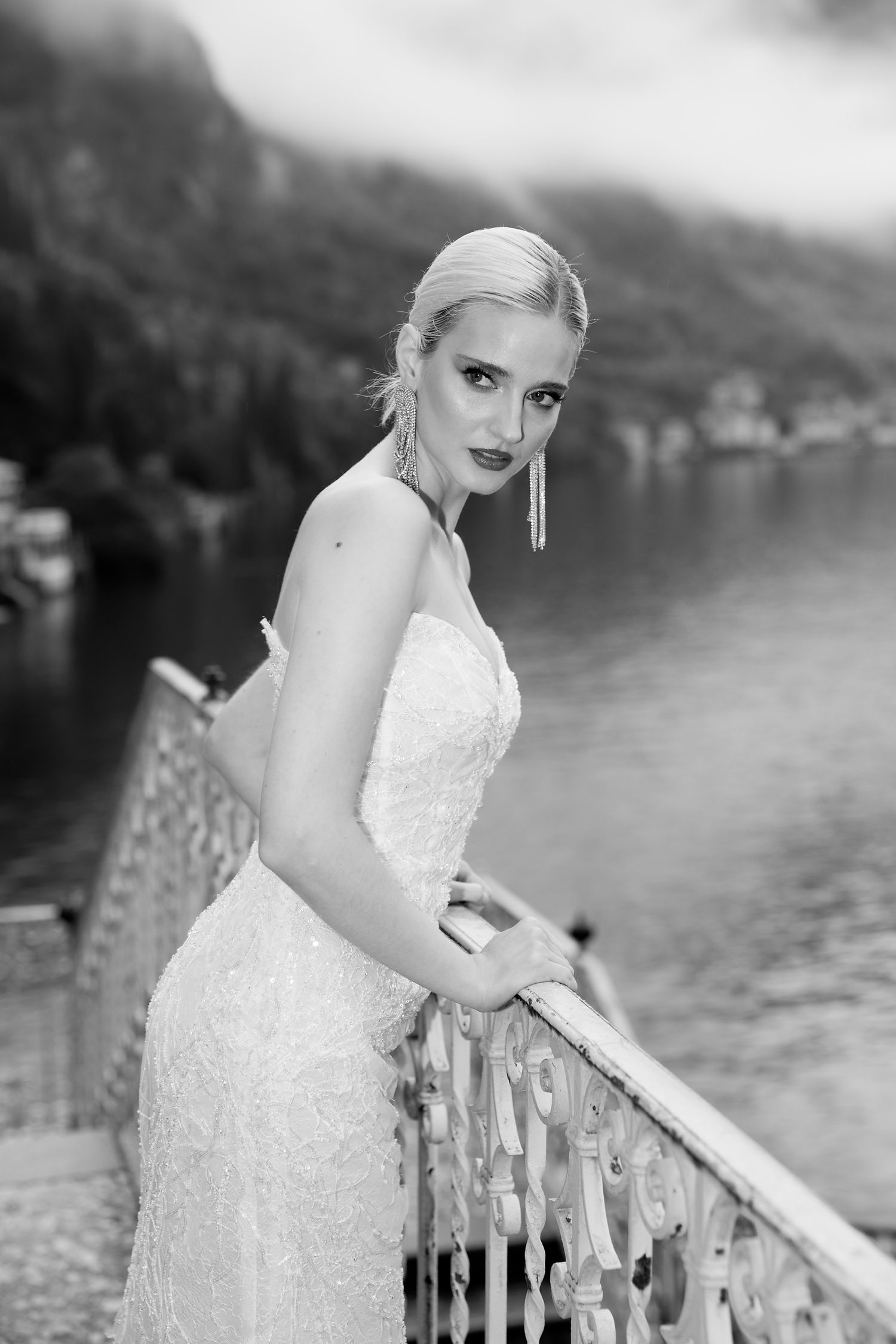 Classic black and white bridal portrait on lakeside terrace with mountain backdrop.