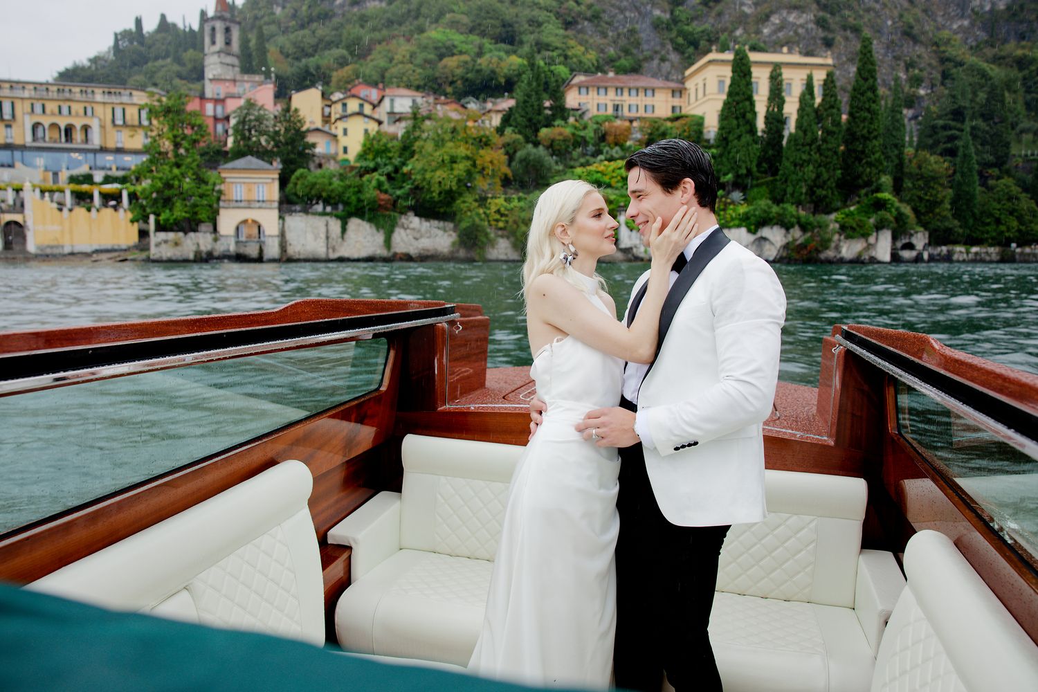 Romantic wedding couple embraces on luxury wooden boat with Italian coastal town in background.