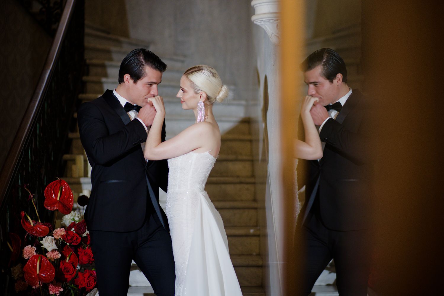 Elegant couple dancing in formal attire near a staircase adorned with red roses.