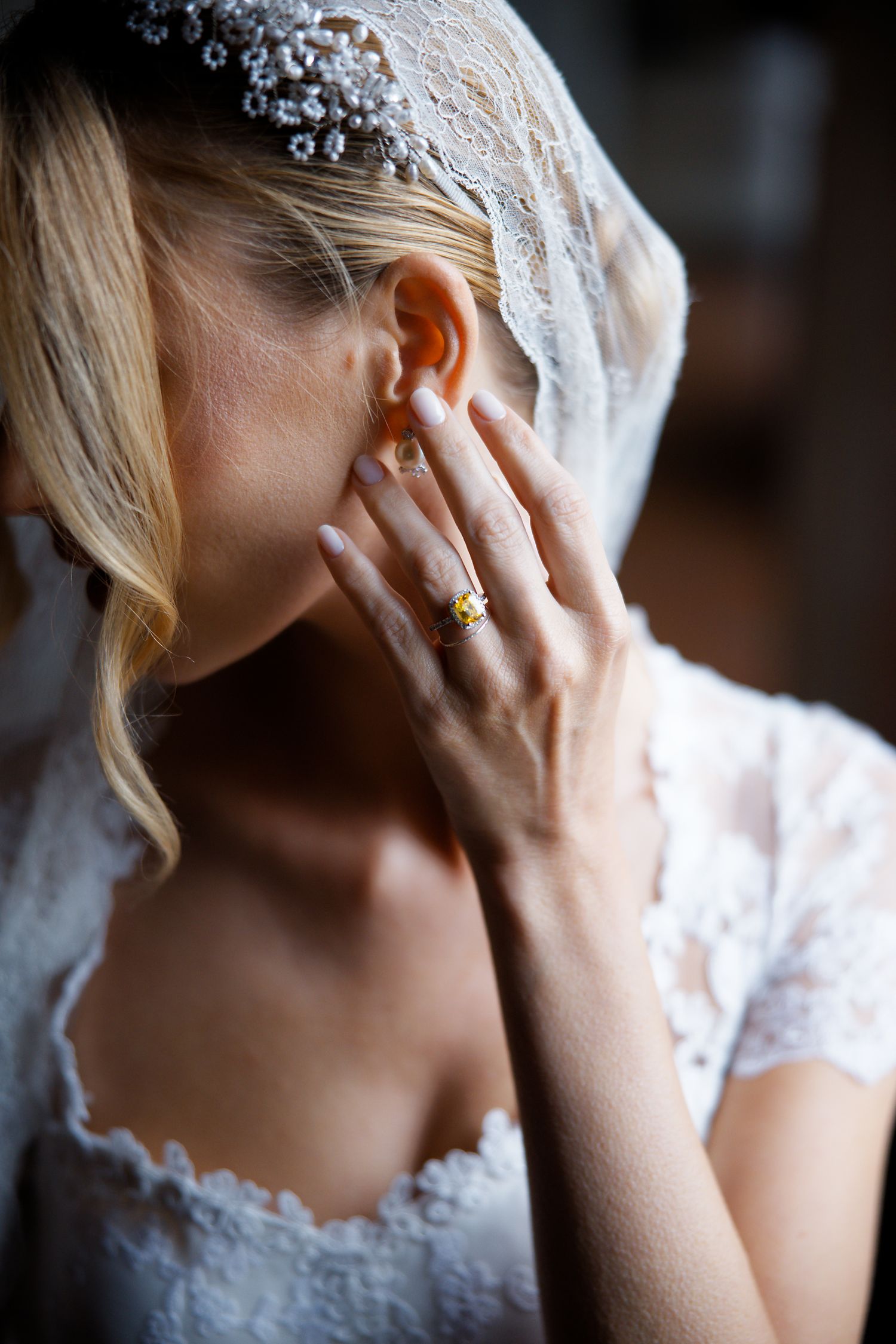 Detail shot of bride wearing delicate crystal headpiece and lace gown with gold ring.