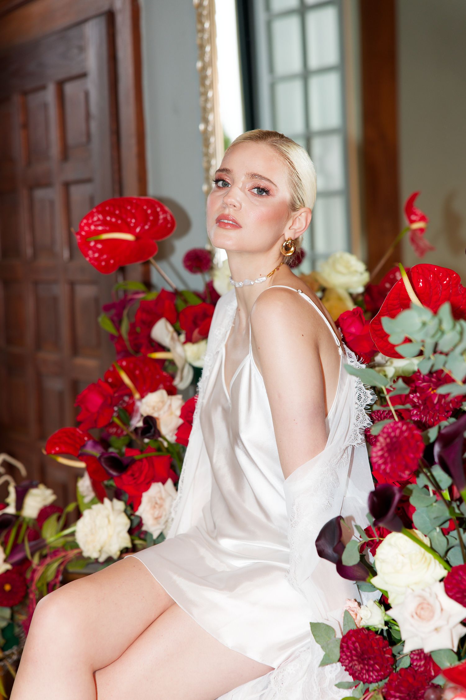 Bridal portrait with red and white floral arrangements in elegant interior setting.