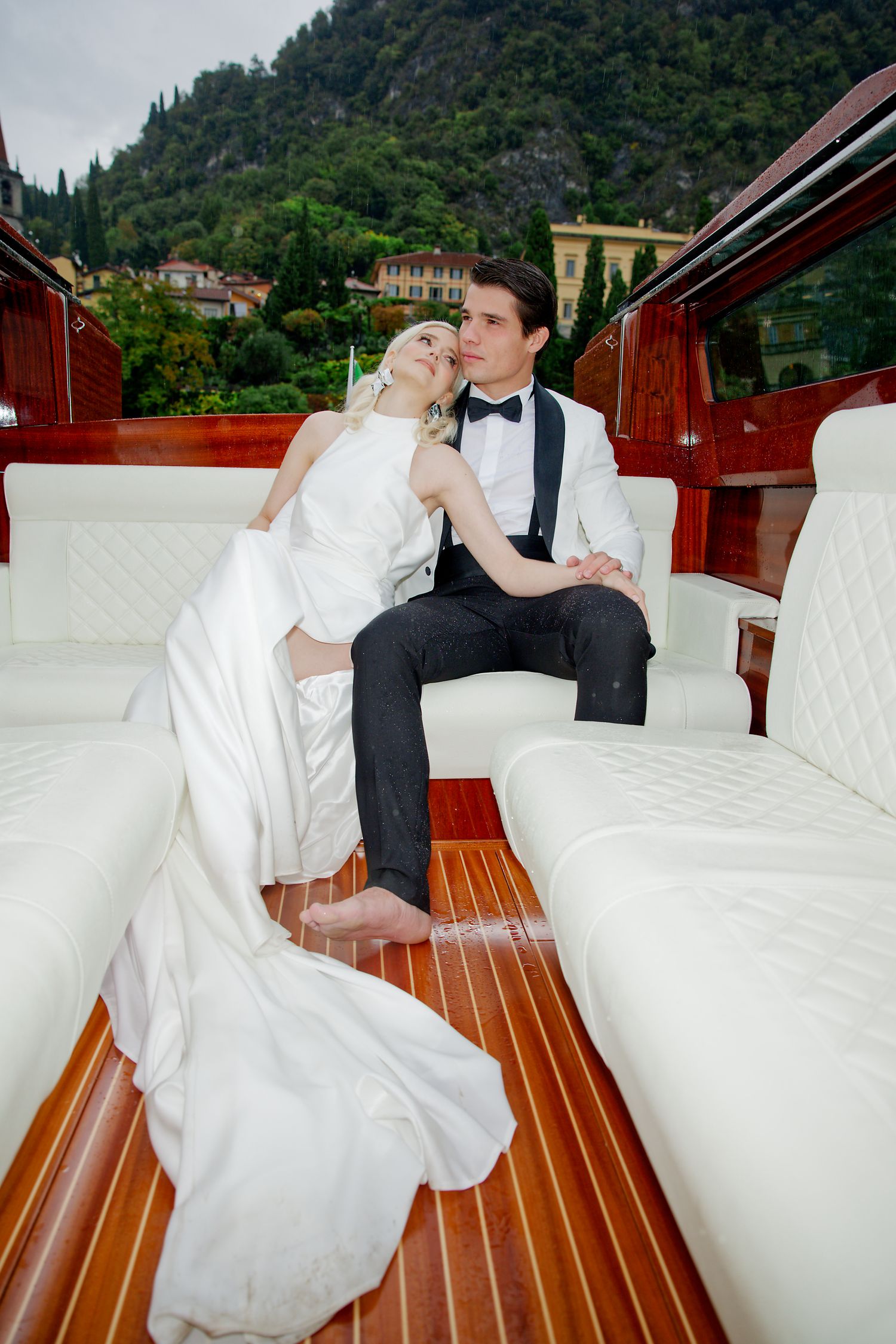 Newlyweds share an intimate moment aboard a luxurious wooden boat with mountains in the distance.