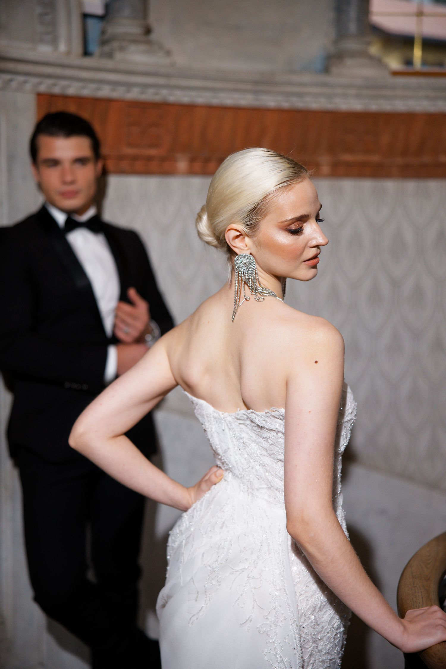 Elegant wedding couple poses in formal attire against textured wall interior.