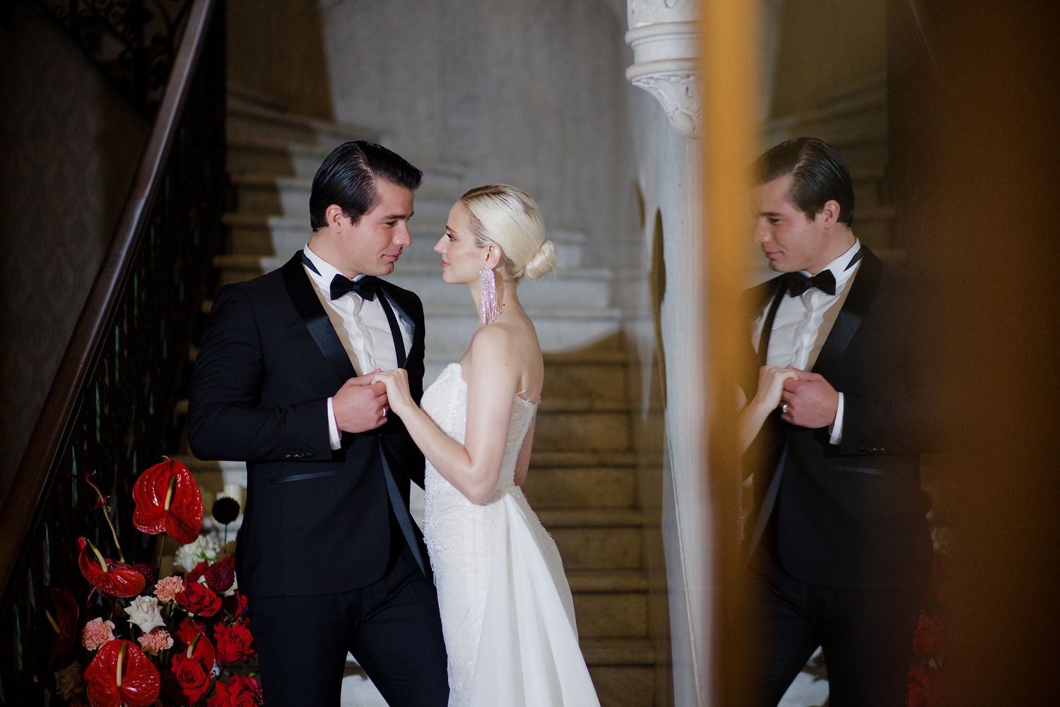 Wedding celebration moment captured in elegant interior with red floral decorations and grand staircase.