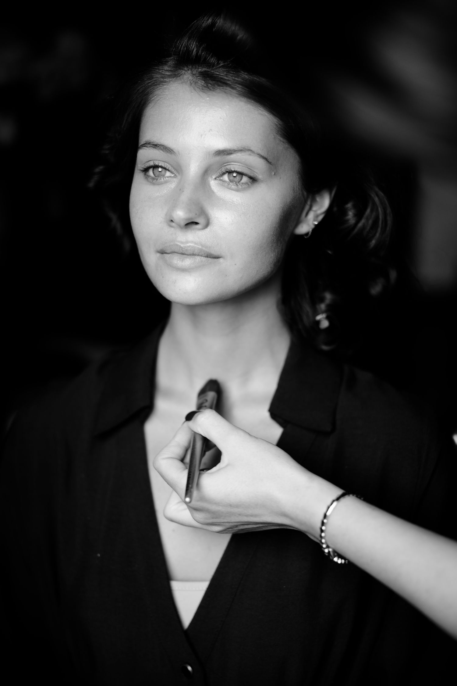 Black and white portrait photo showing someone getting makeup applied by an artist's hand with bracelet.