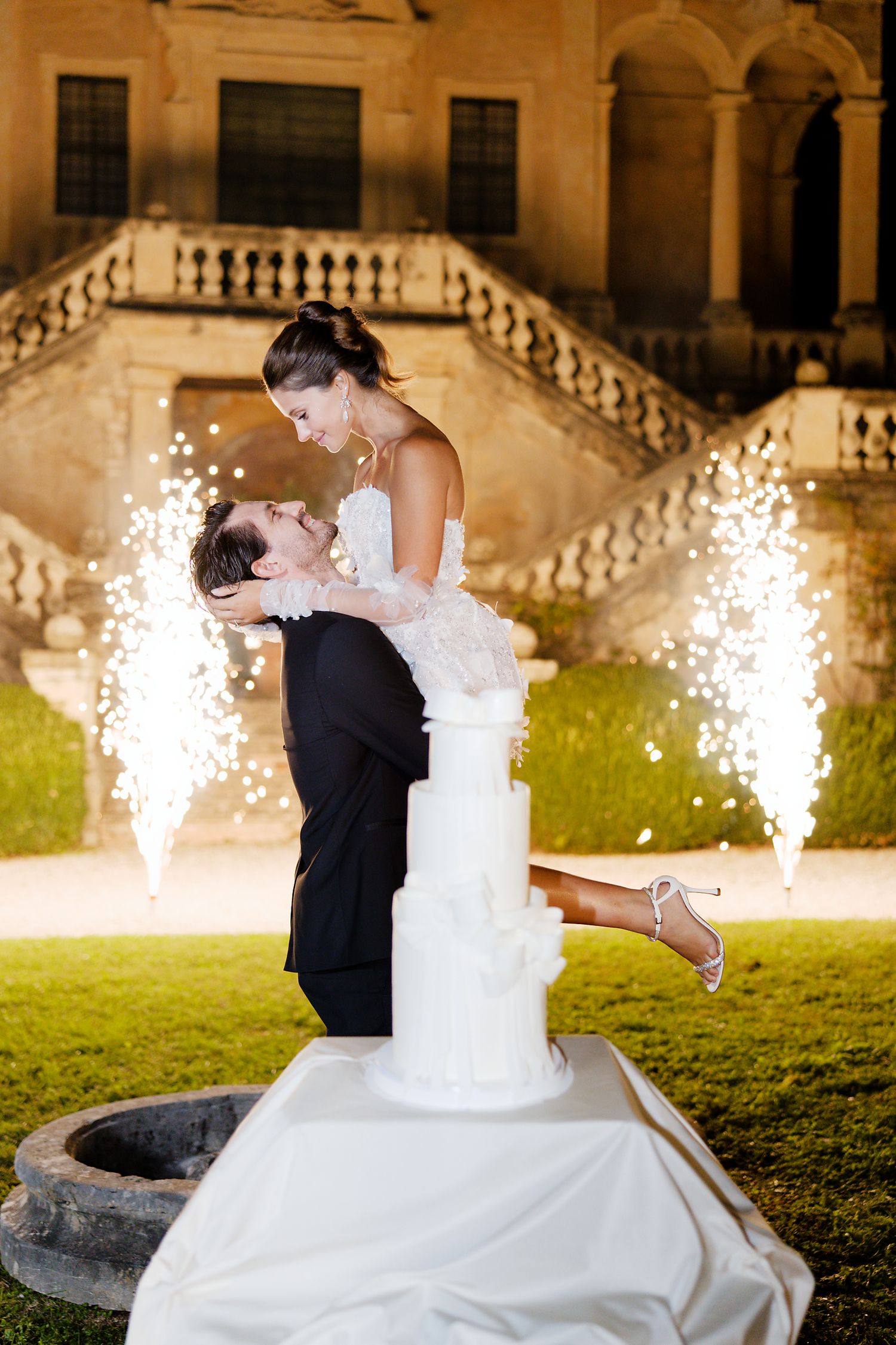 Romantic wedding moment captured with sparklers illuminating the night at villa entrance.