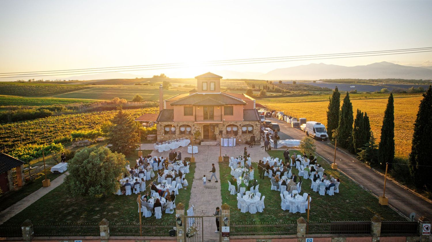 Aerial view of a Tuscan villa wedding reception at sunset with guests seated at outdoor tables.
