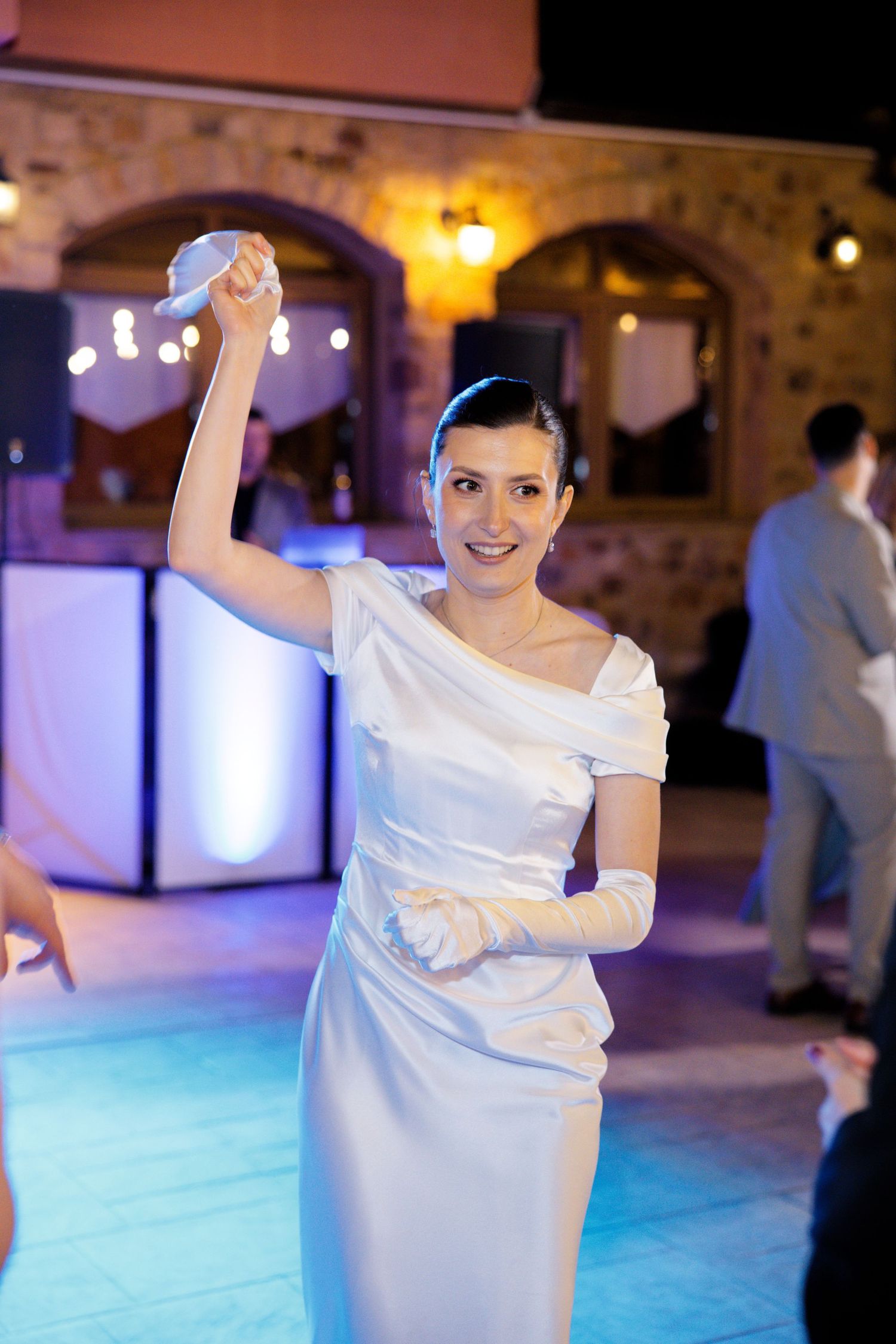 Bride dancing in off-shoulder white dress on illuminated dance floor with purple lighting.