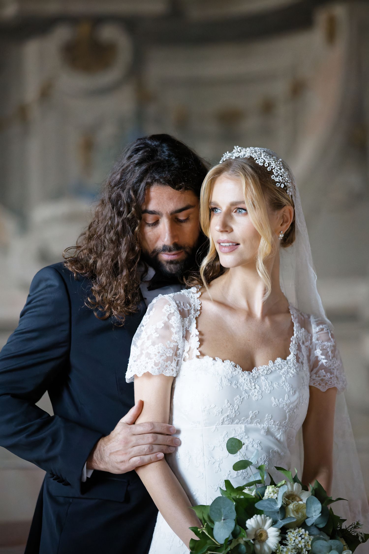 A romantic wedding portrait of a couple posing together, with the bride holding a bouquet of greenery and white flowers.