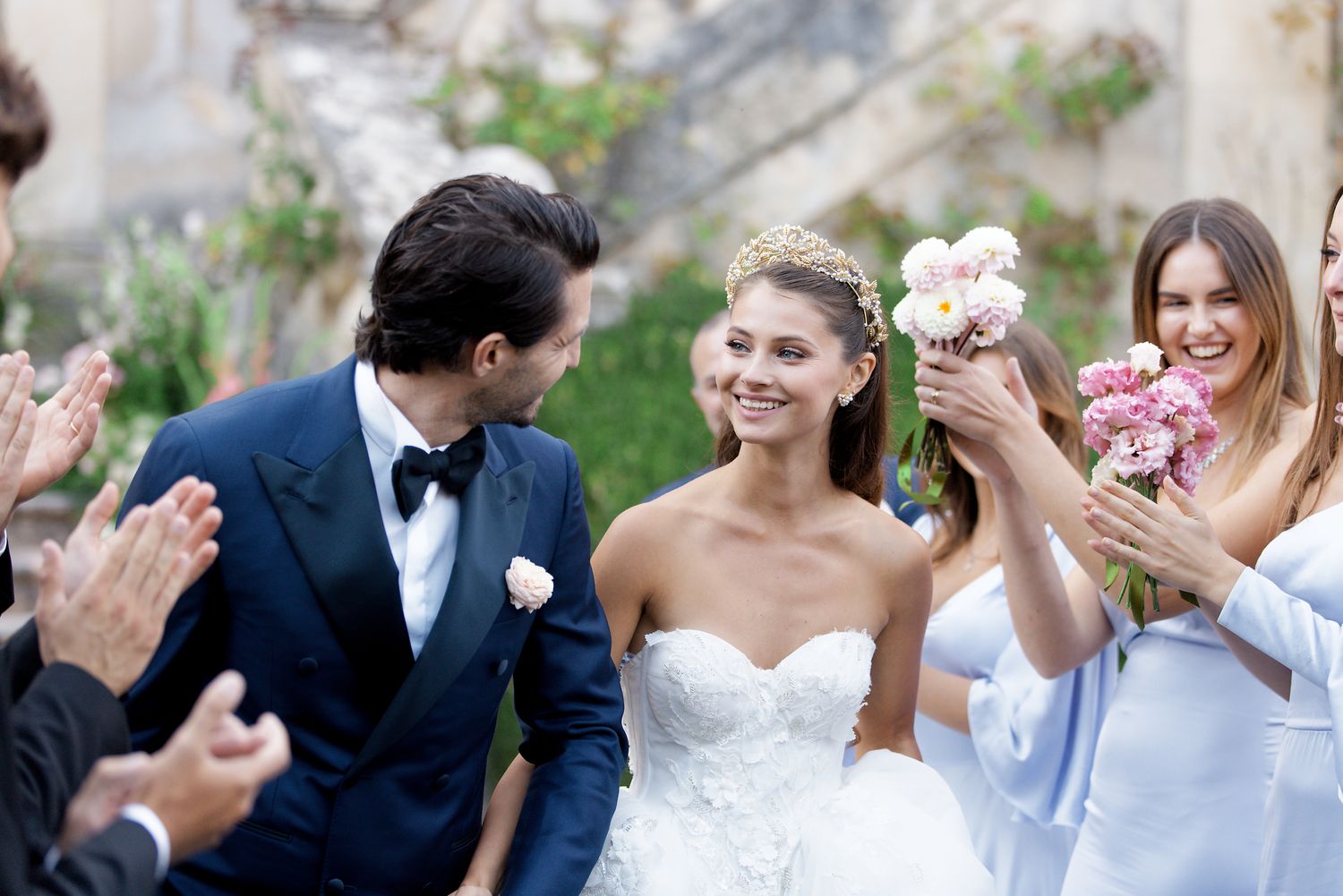 Wedding celebration in an outdoor garden setting with floral decorations and guests throwing confetti.