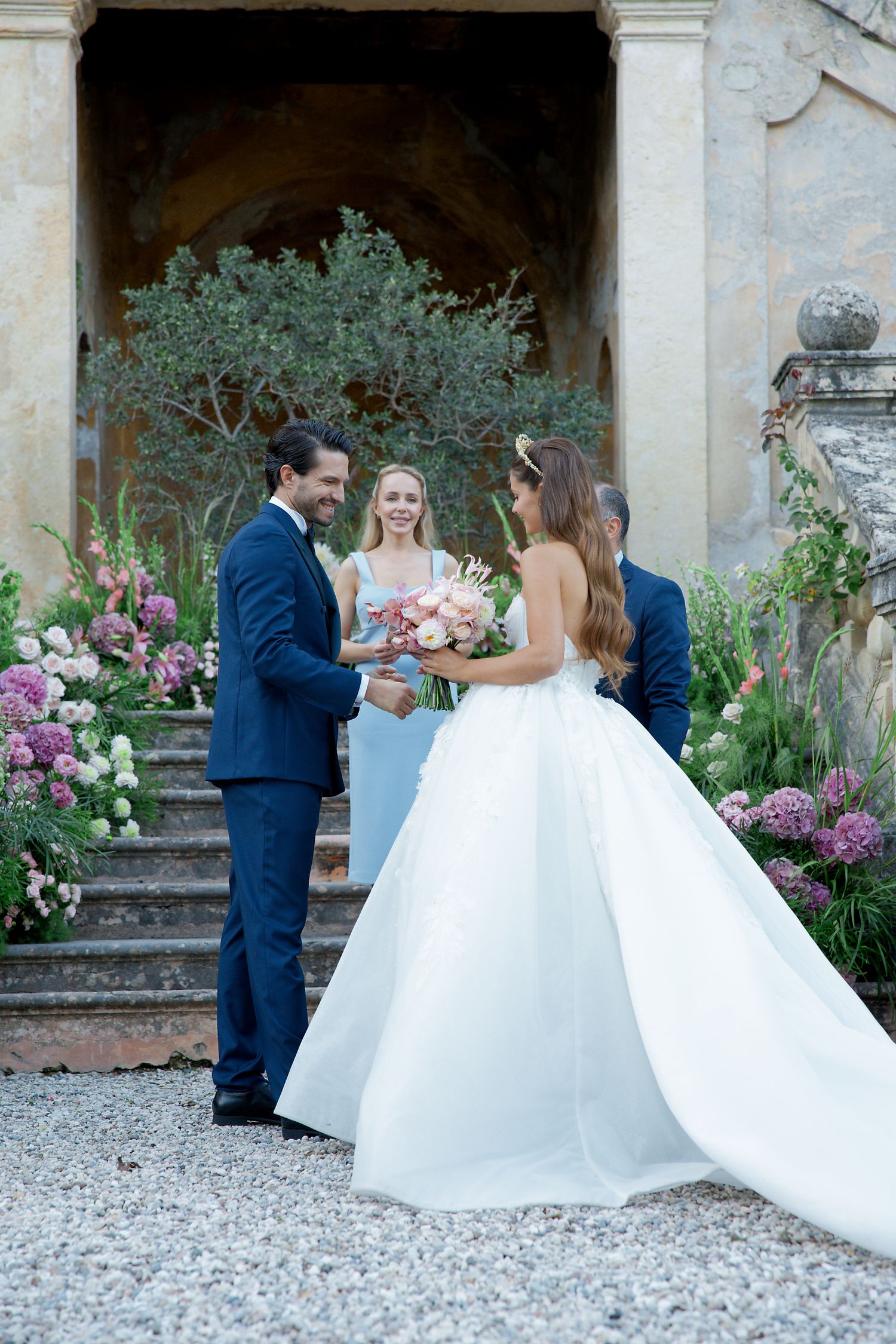 Elegant wedding ceremony taking place on ornate stone steps decorated with vibrant pink flowers and greenery.