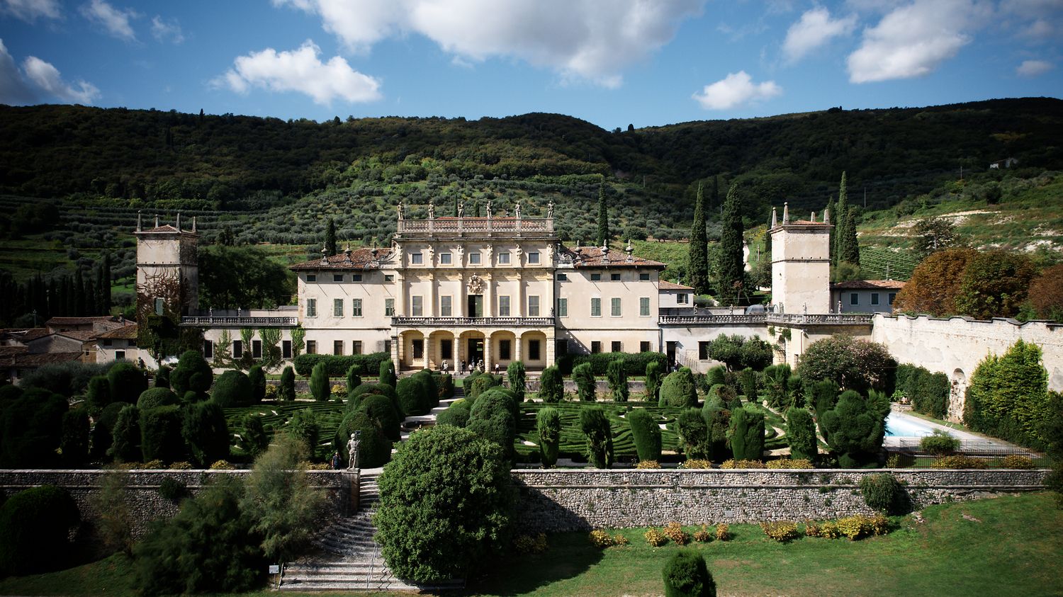 Grand Renaissance villa with manicured gardens nestled in Tuscan hillside landscape.