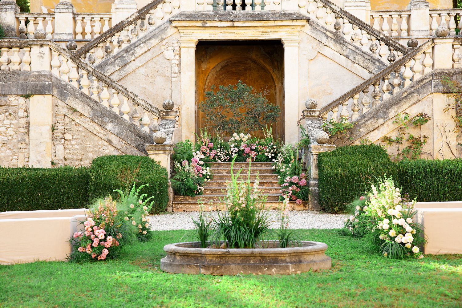 An elegant garden staircase features ornate stone details and floral arrangements leading to a decorative alcove.