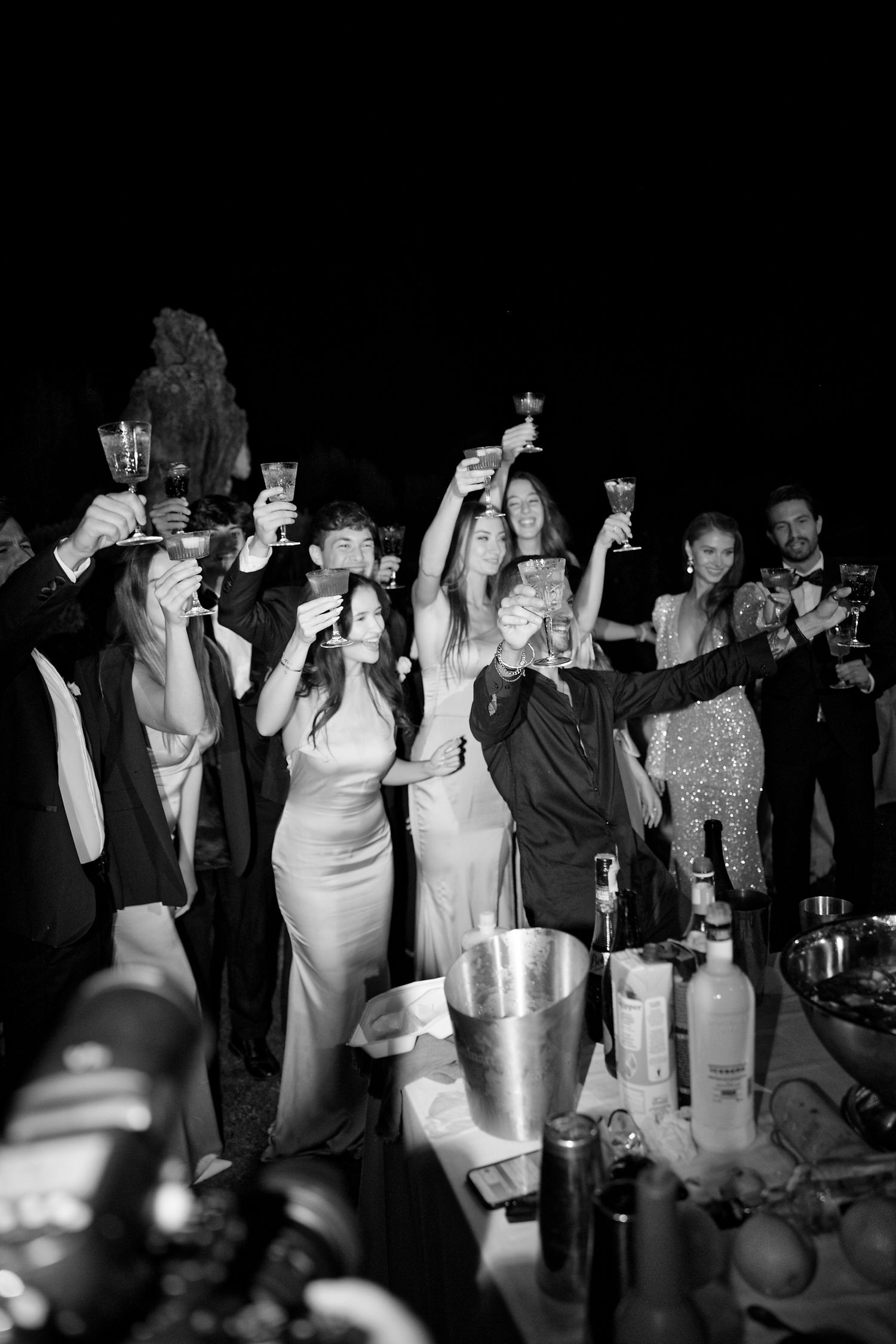 Party guests raise glasses in celebration at nighttime outdoor event.