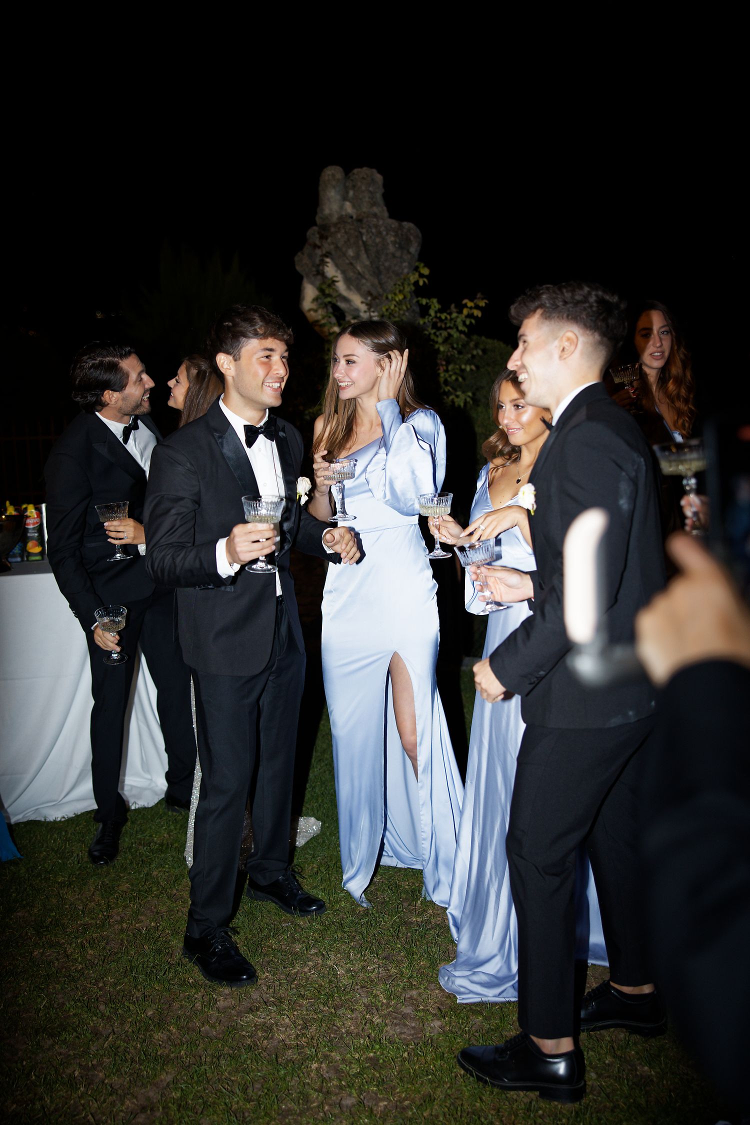 Elegant evening party outdoors with guests in formal attire mingling and socializing at night.