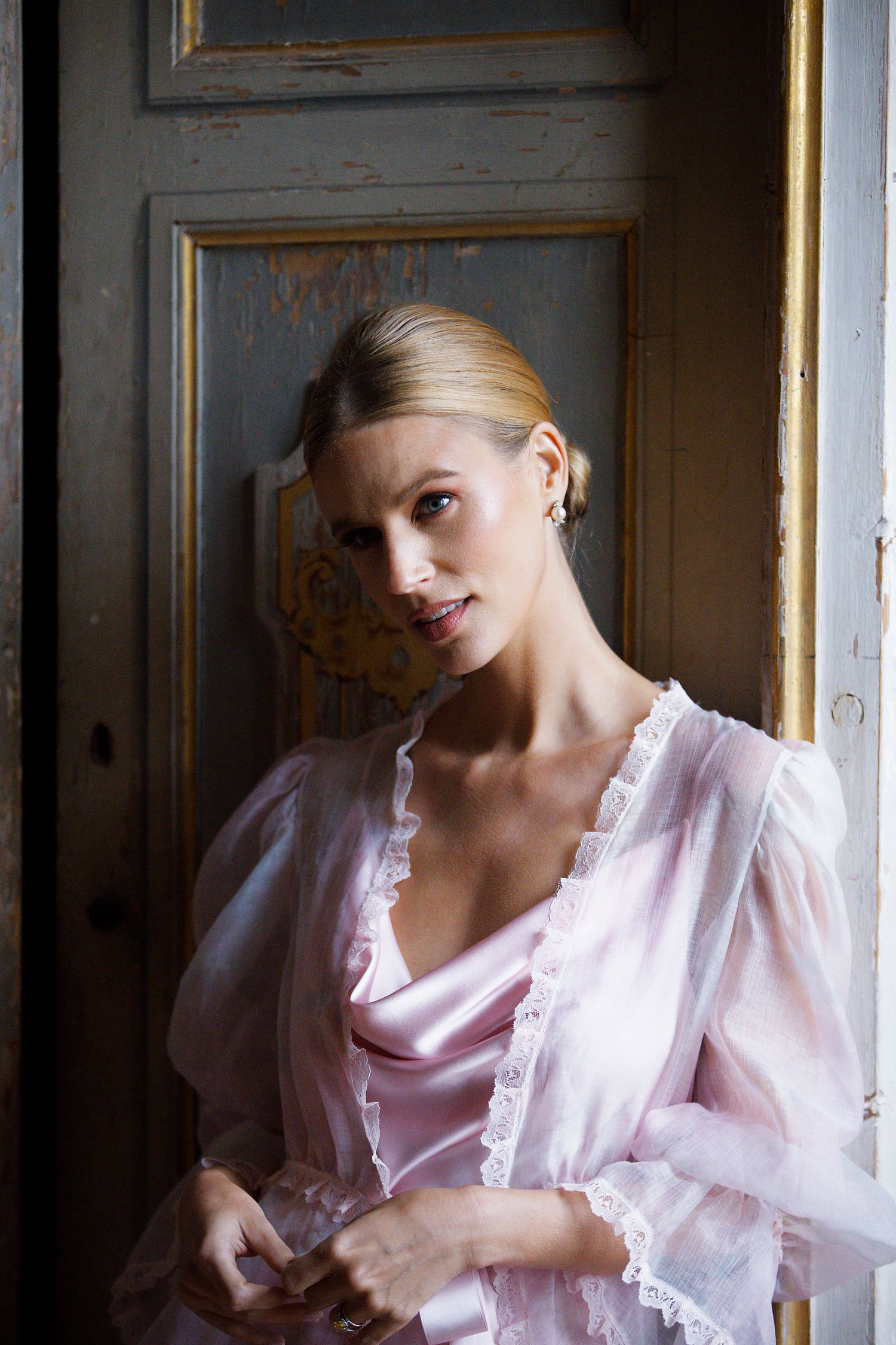 Classic portrait in pink satin and lace robe against vintage doorframe with natural lighting.