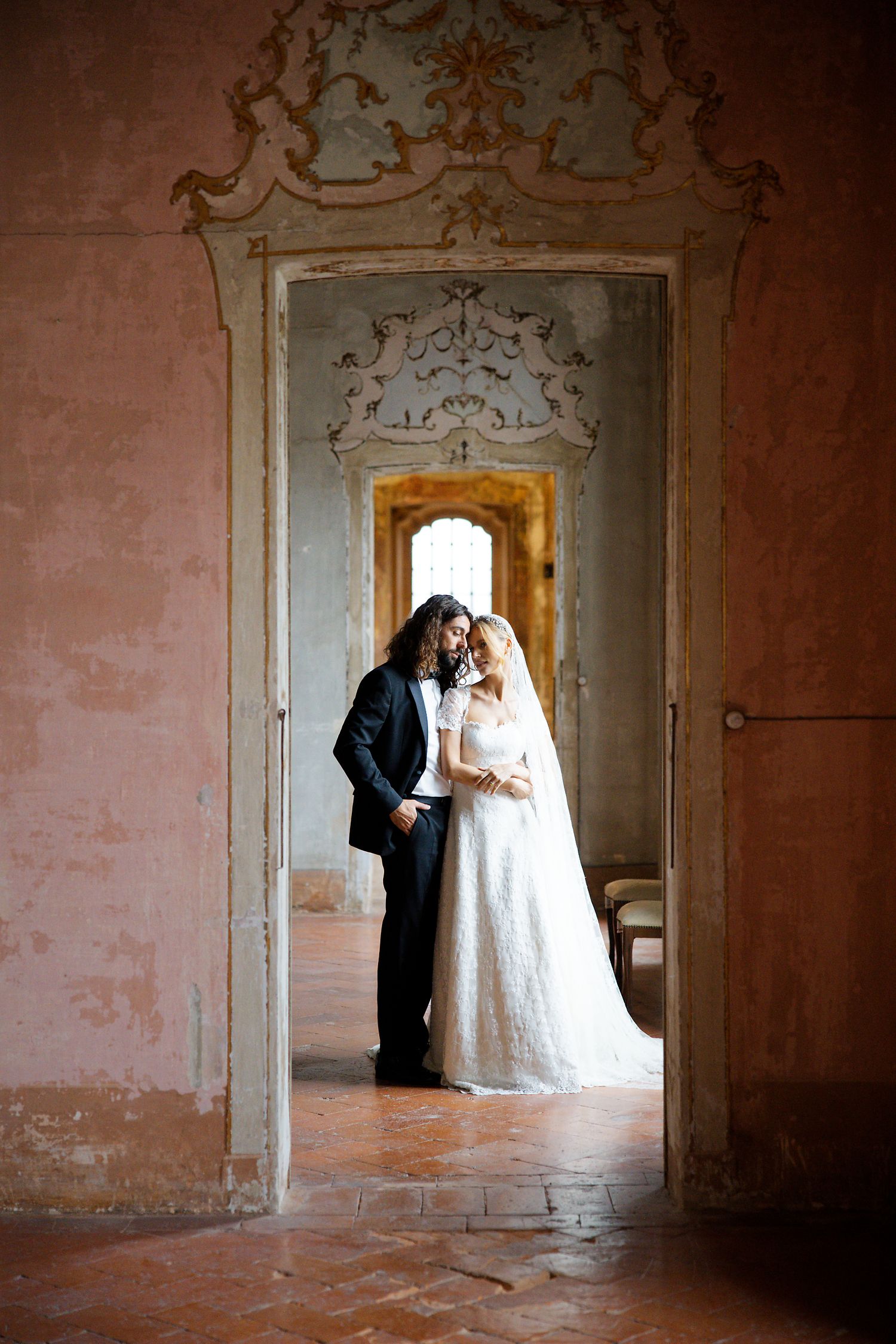 Wedding couple standing in an ornate doorway of a historic building with pink walls and decorative molding.