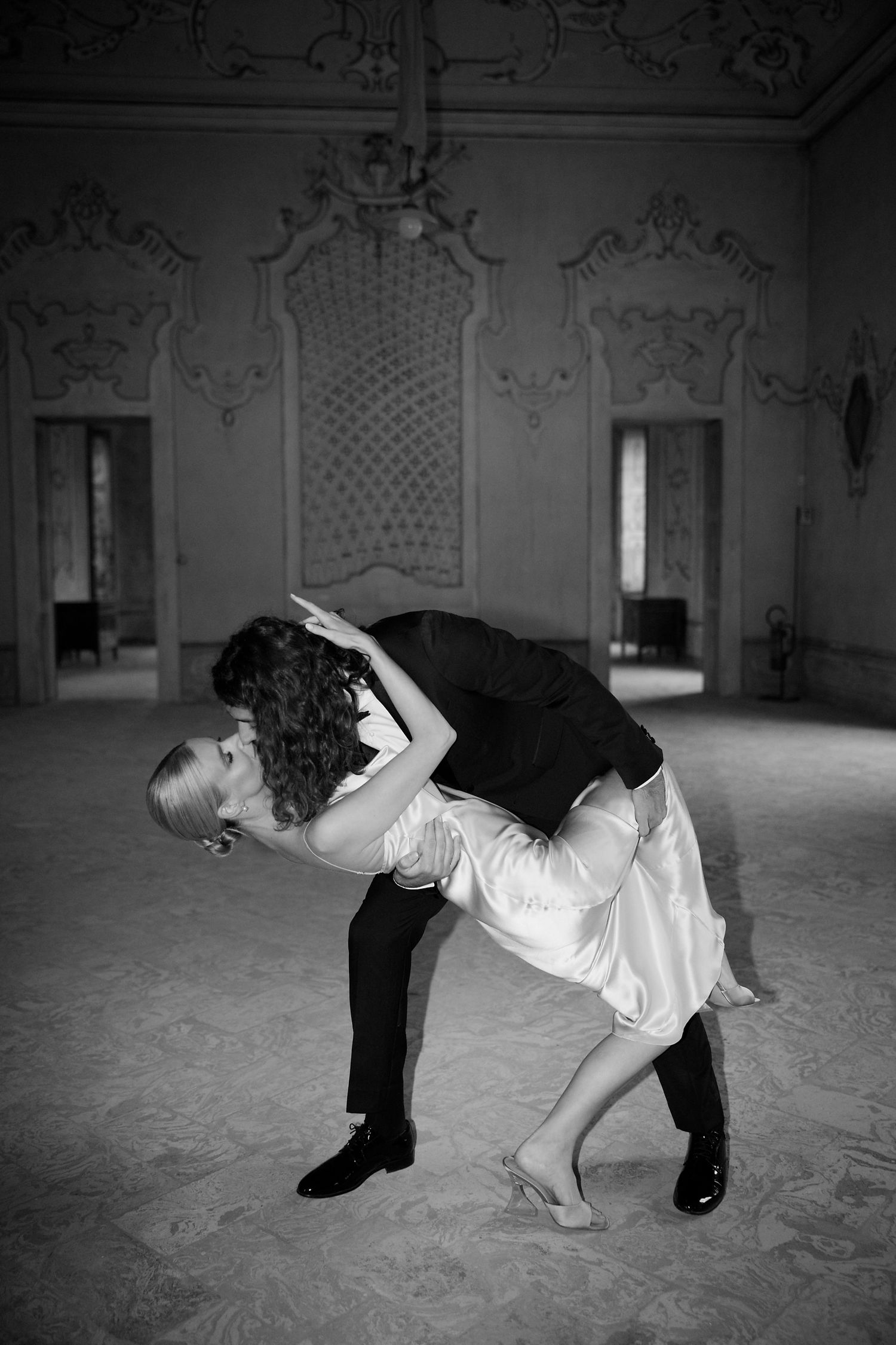 A couple performs a romantic dance dip in formal attire within an ornately decorated ballroom.